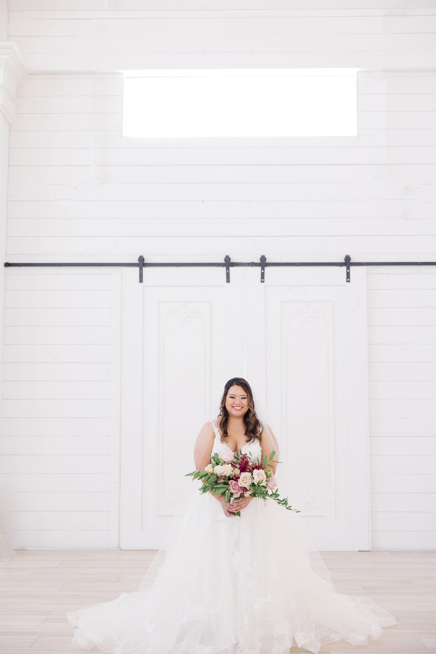 bride stands in front of sliding wooden door at The Nest at Ruth Farms with bouquet of pink flowers 