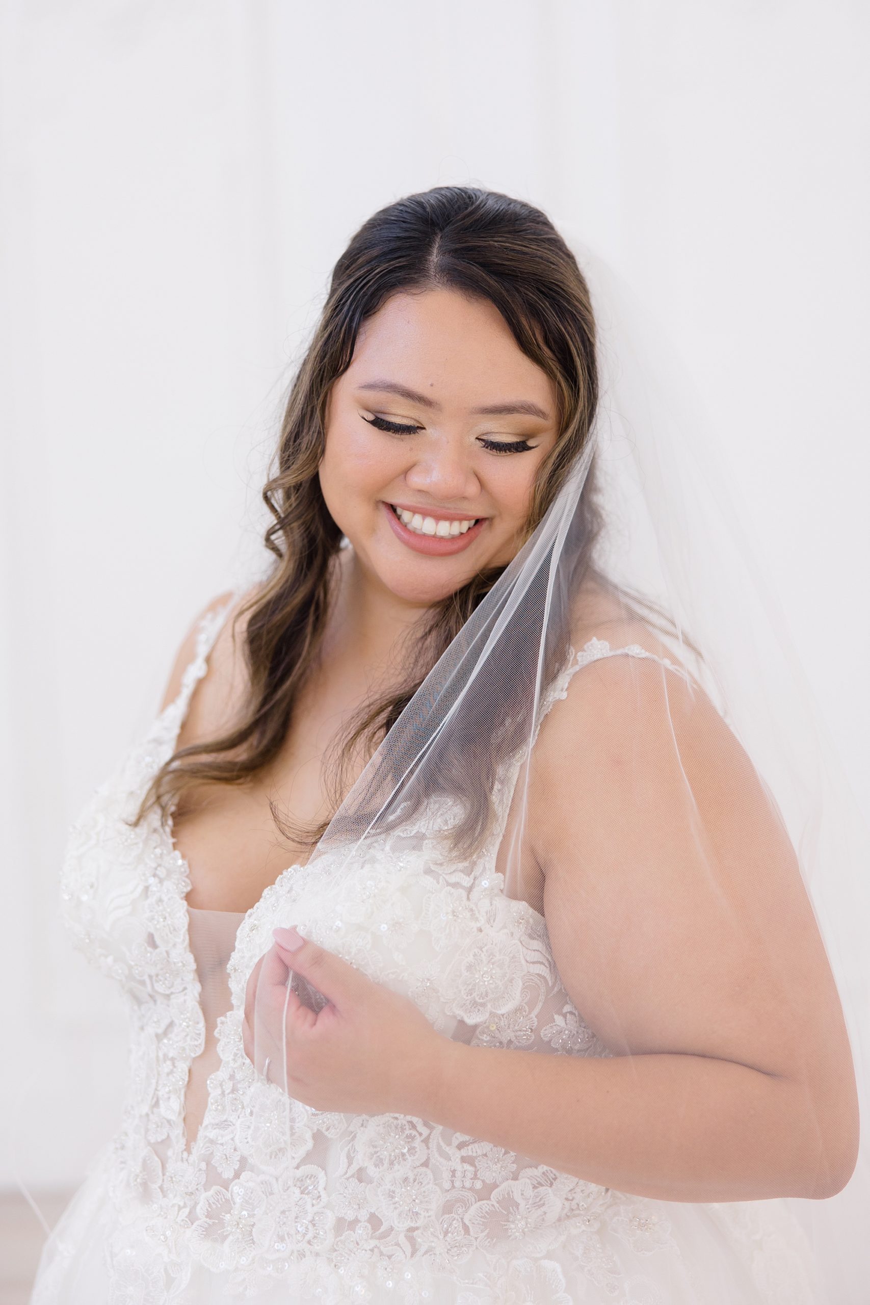 bride smiles wrapping veil around her shoulders at The Nest at Ruth Farms