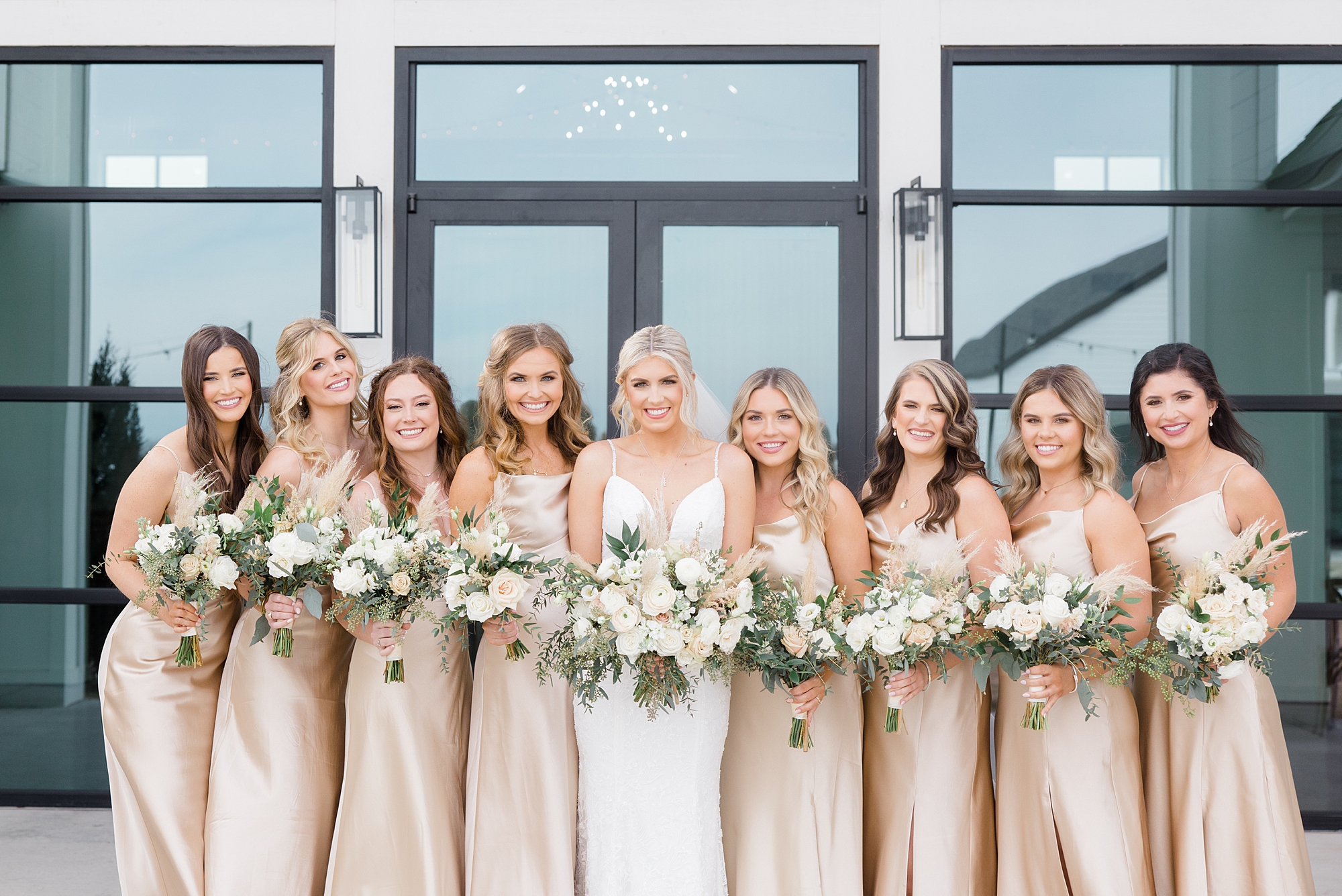 bride stands with bridesmaids in champagne gowns with pastel bouquets 
