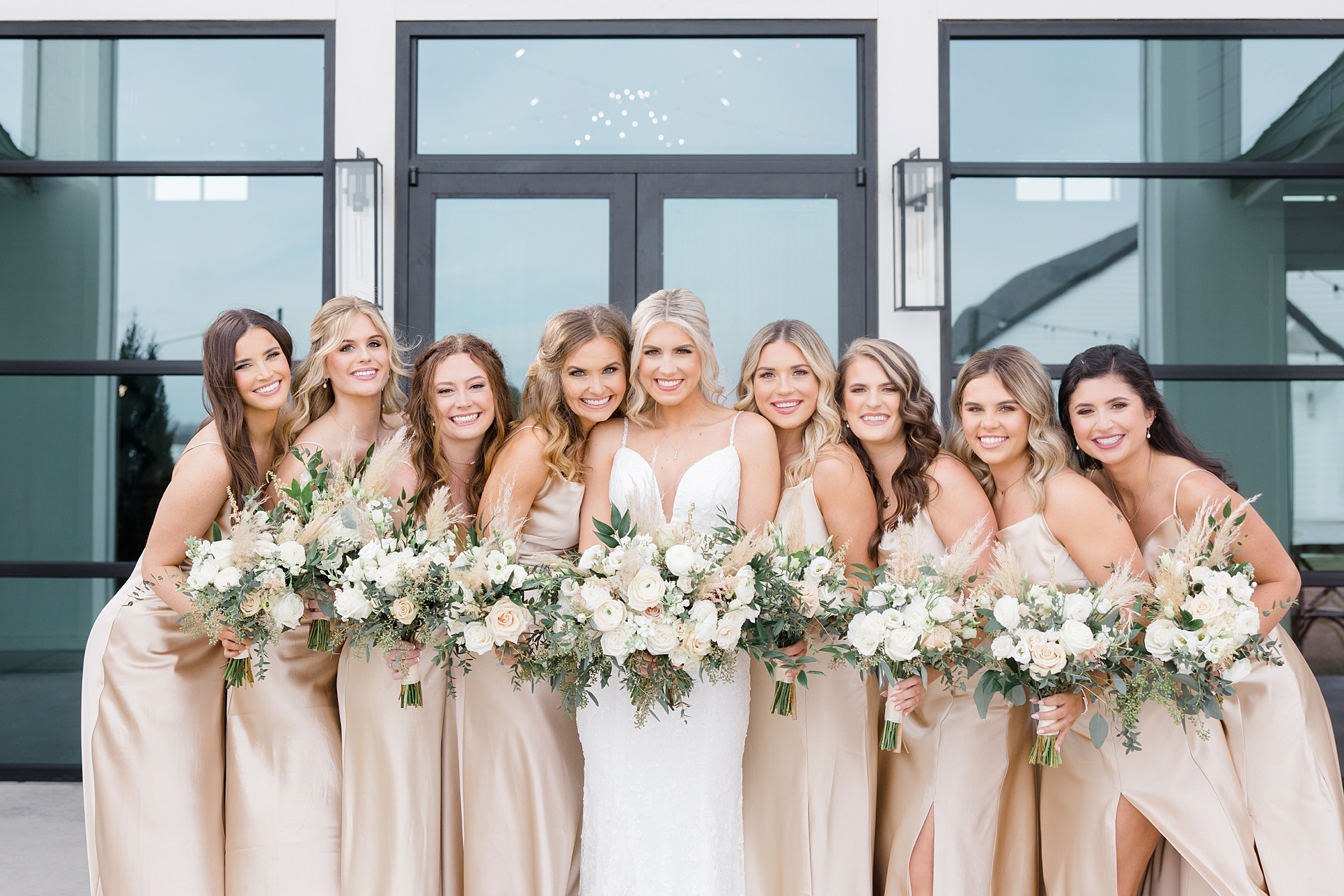 bridesmaids in pastel champagne gowns hug next to bride with bouquets 