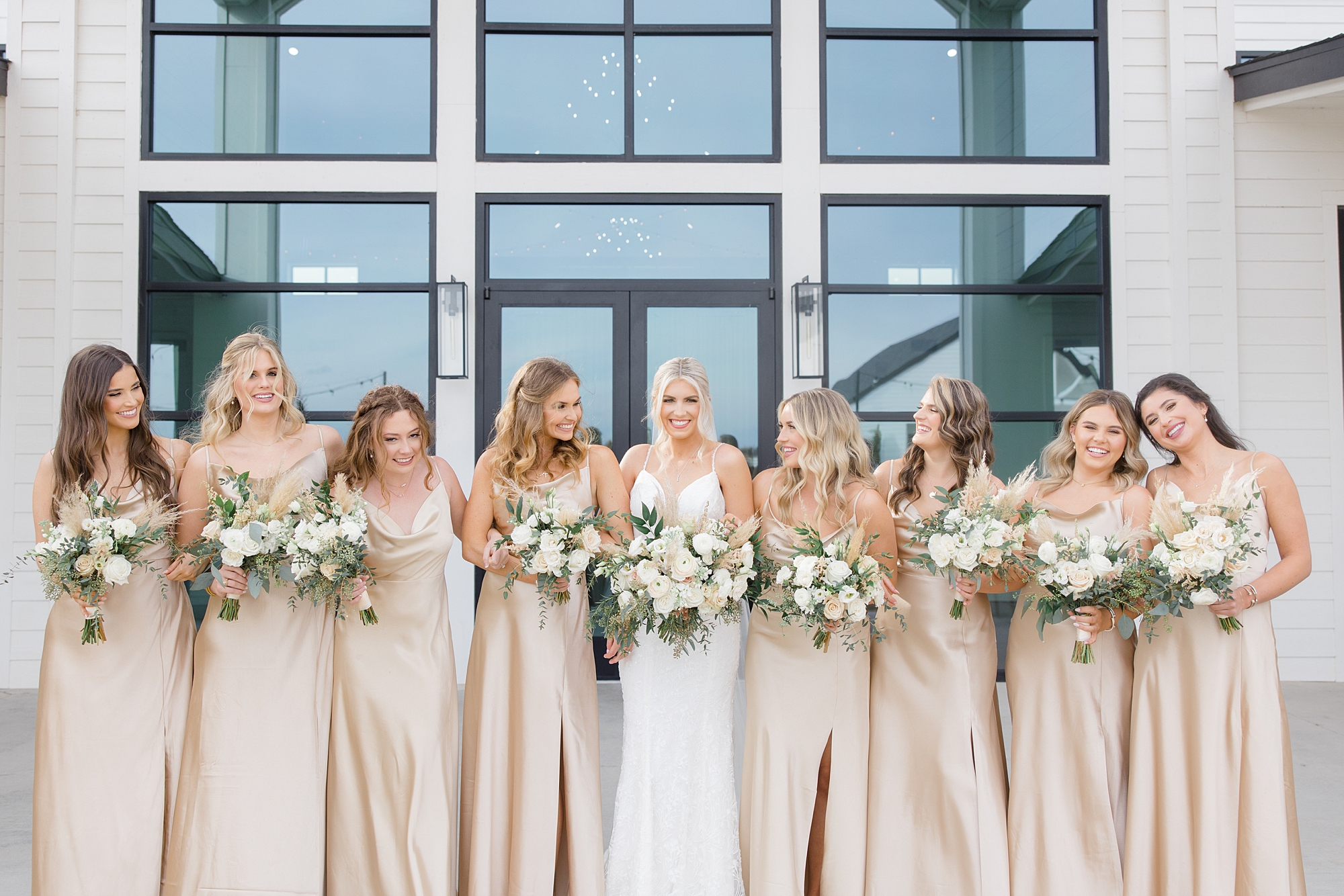 bride poses with bridesmaids in champagne gowns with pastel bouquets 