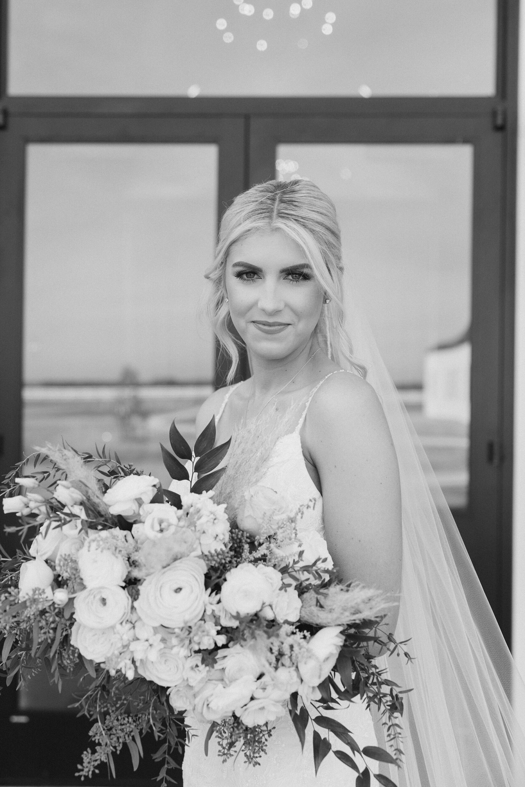 black and white portrait of bride holding bouquet and veil draped behind her 