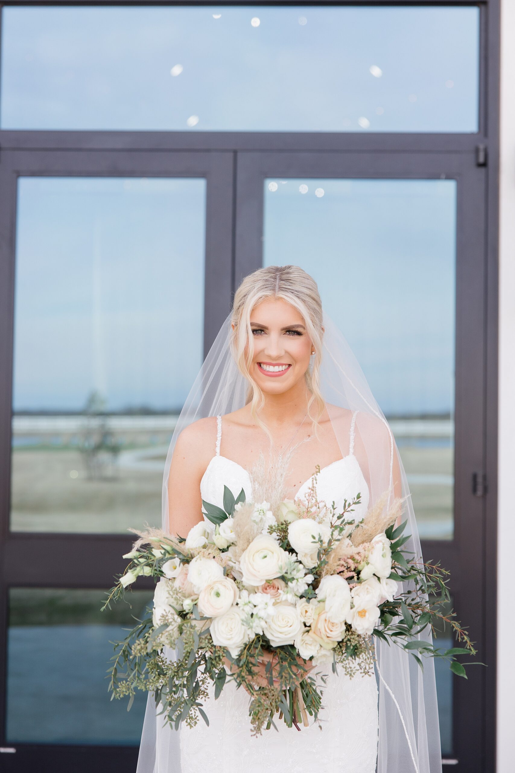 bride holds bouquet of ivory flowers outside windows at The Gardenia