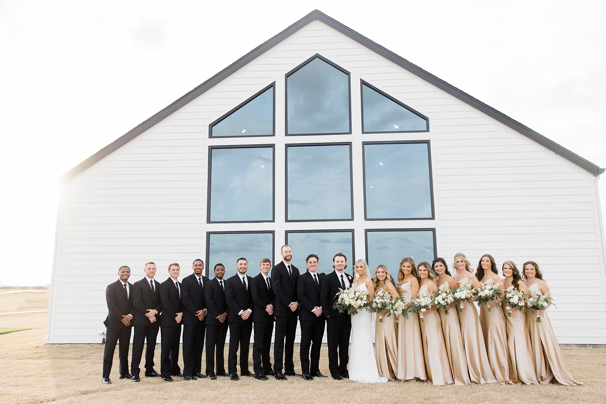 bride and groom pose with wedding party in black suits and champagne gowns outside The Gardenia