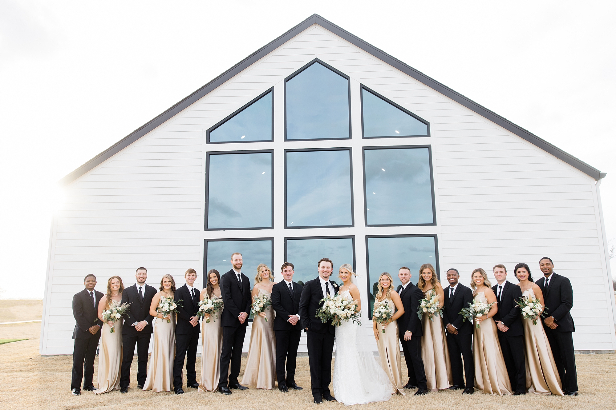 newlyweds pose with wedding party by glass windows at The Gardenia