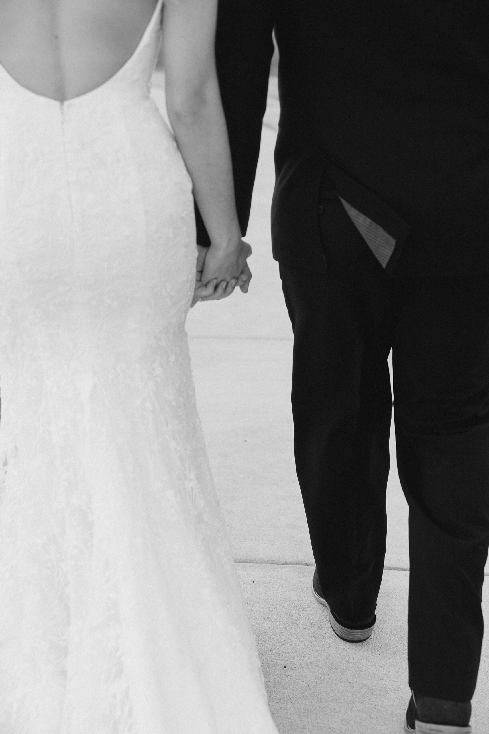 newlyweds hold hands walking on sidewalk 