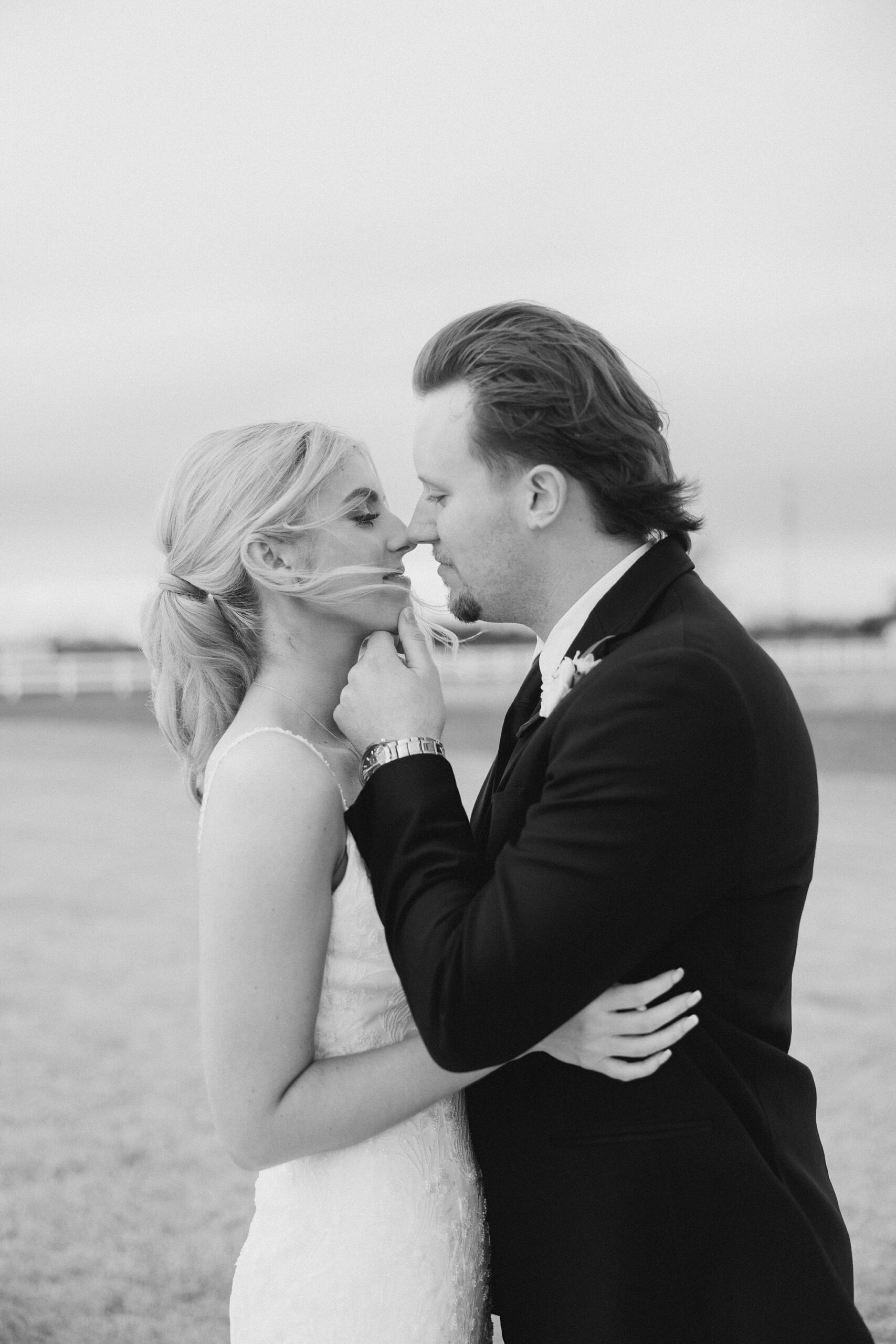 black and white portrait of groom leaning to kiss bride with wind blowing around them 