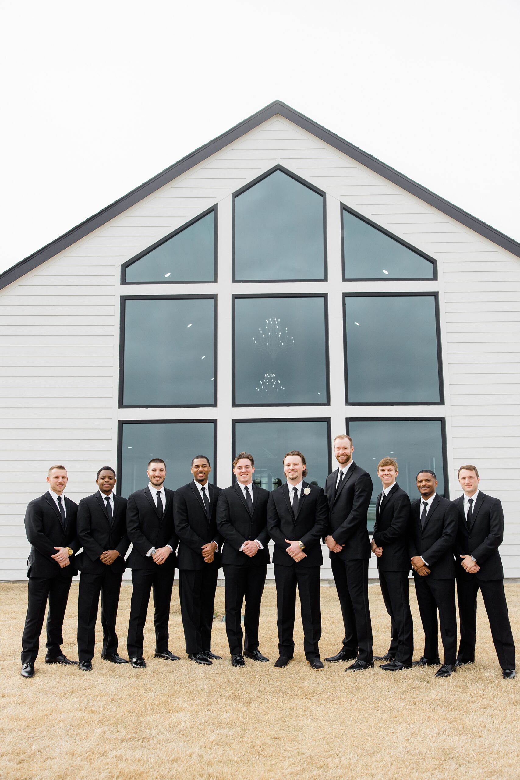 groom stands with groomsmen by windows at The Gardenia