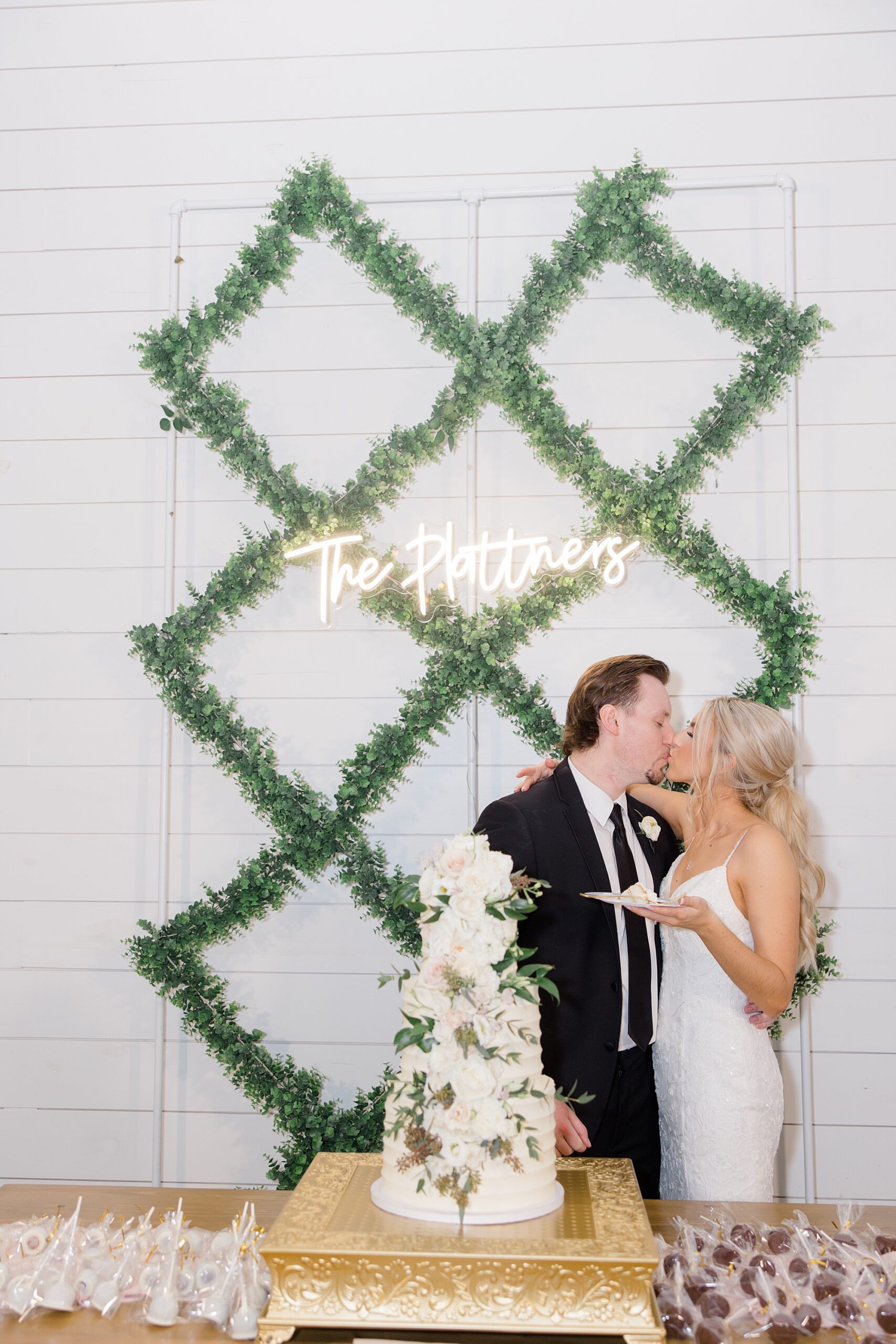 bride and groom cut wedding cake by wall with greenery accents