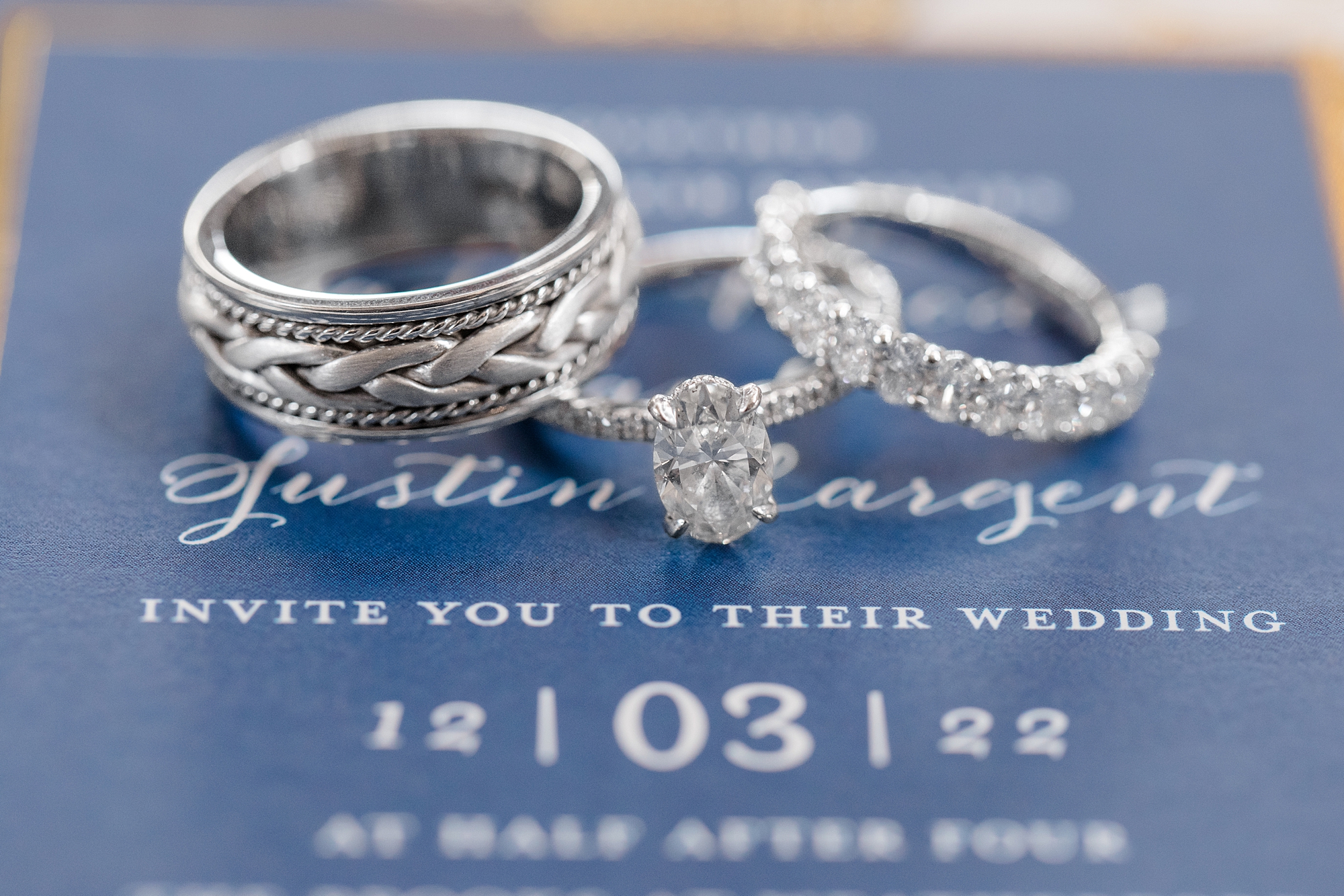 three wedding bands lay on blue invitation suite 