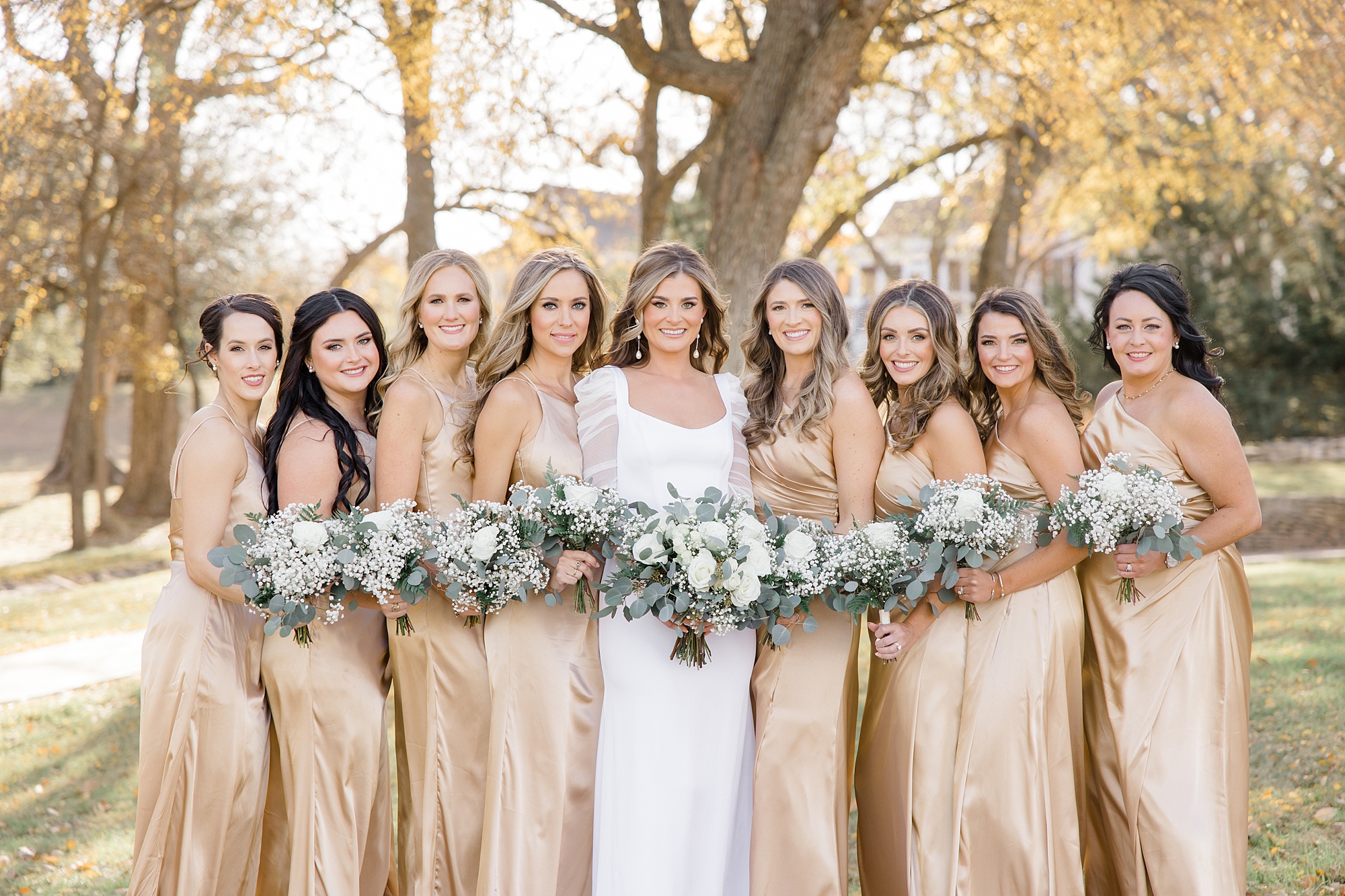 bride poses with bridesmaids in gold gowns with all-white bouquets 