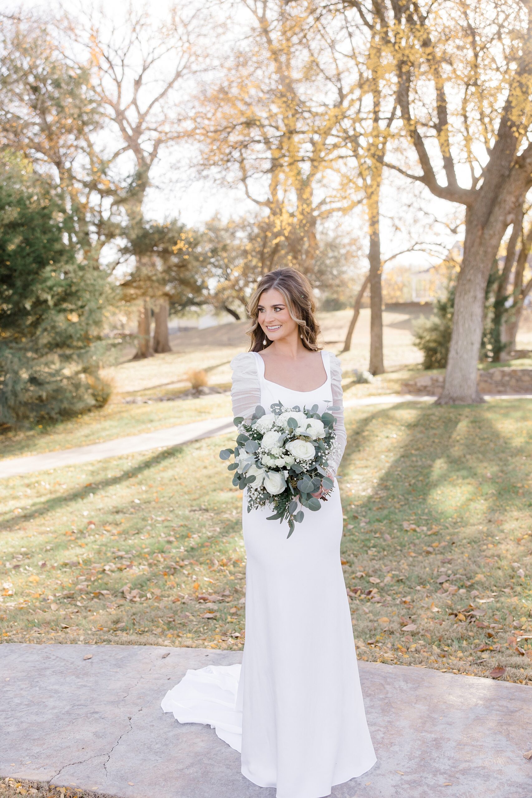 winter bride holds bouquet in front of stomach looking over shoulder 