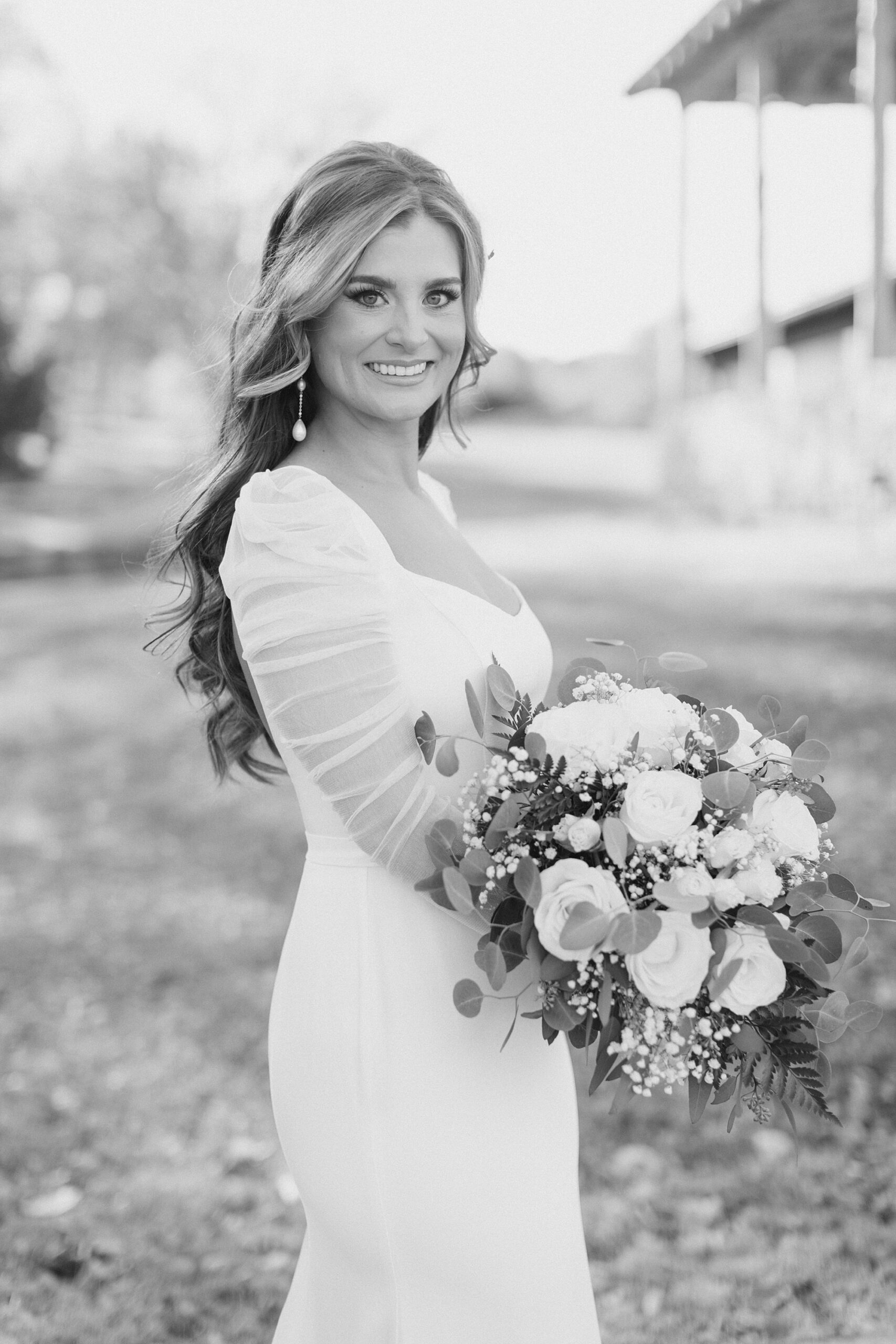 bride smiles holding bouquet in front of hips in wedding gown with long sleeves 
