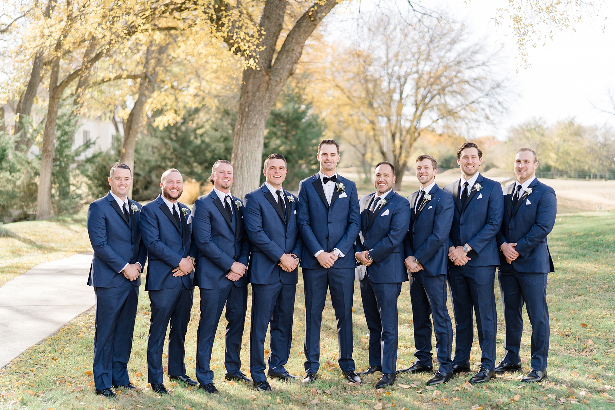 groom poses with groomsmen in navy suits with hands in front of jackets 