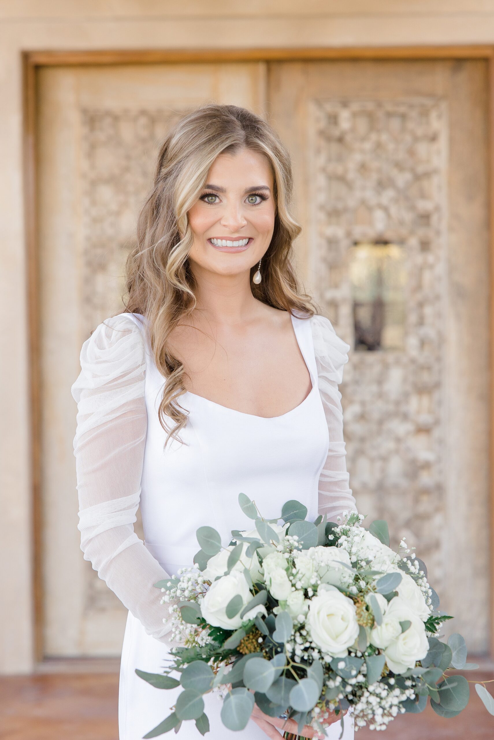 bride in winter wedding gown with long sleeves smiles holding bouquet of white roses 