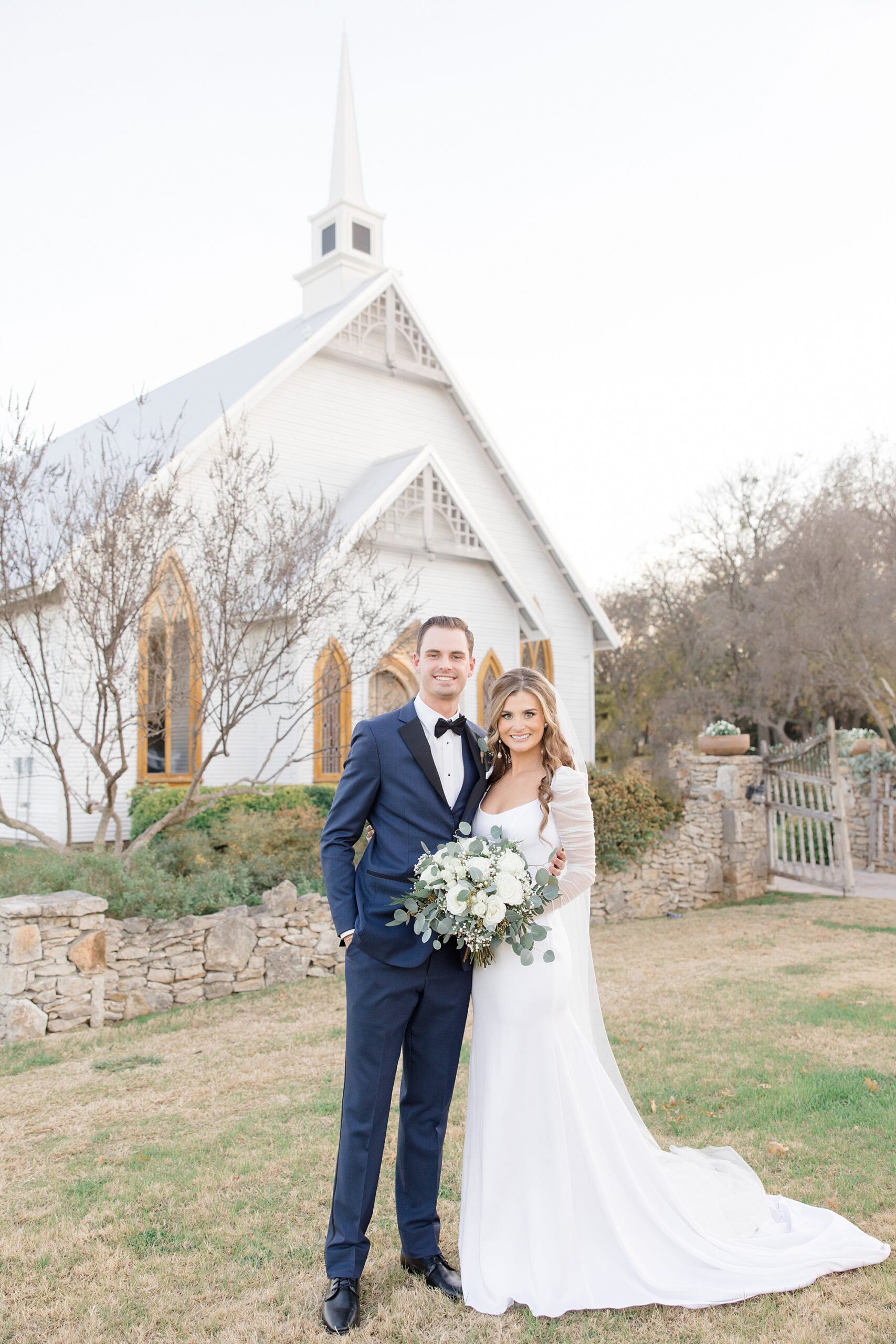 bride and groom pose outside white chapel in Texas 