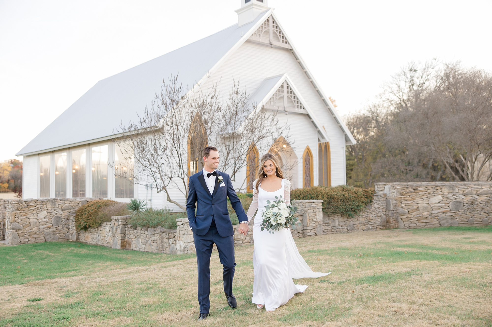 bride and groom walk outside white chapel at The Brooks at Weatherford