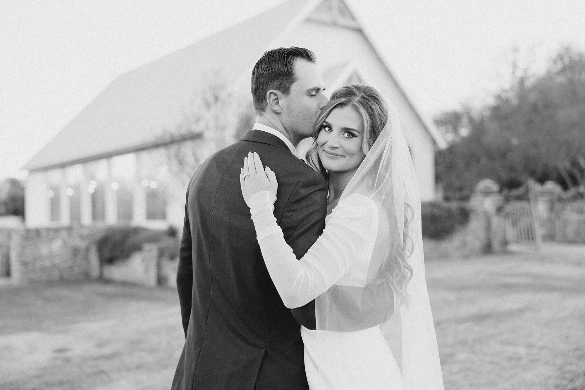 black and white portrait of bride and groom hugging by chapel at The Brooks at Weatherford