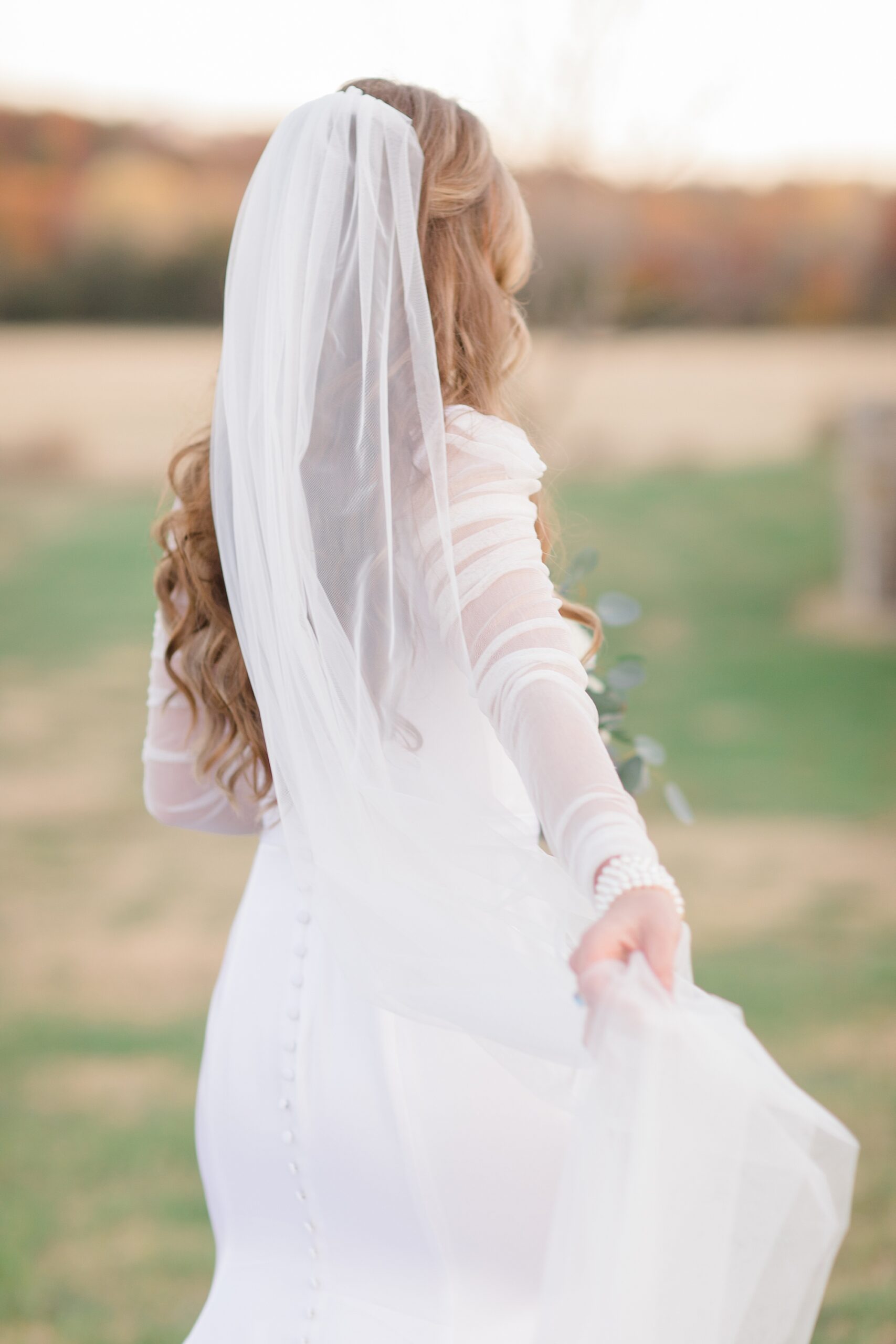 bride holds skirt of wedding gown walking through field 