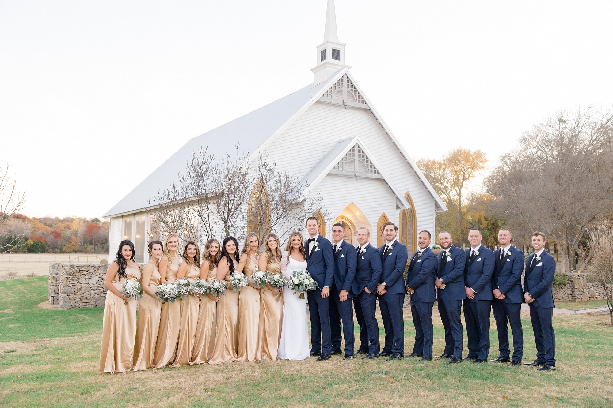 bride and groom stand with wedding party in gold gowns and navy suits 