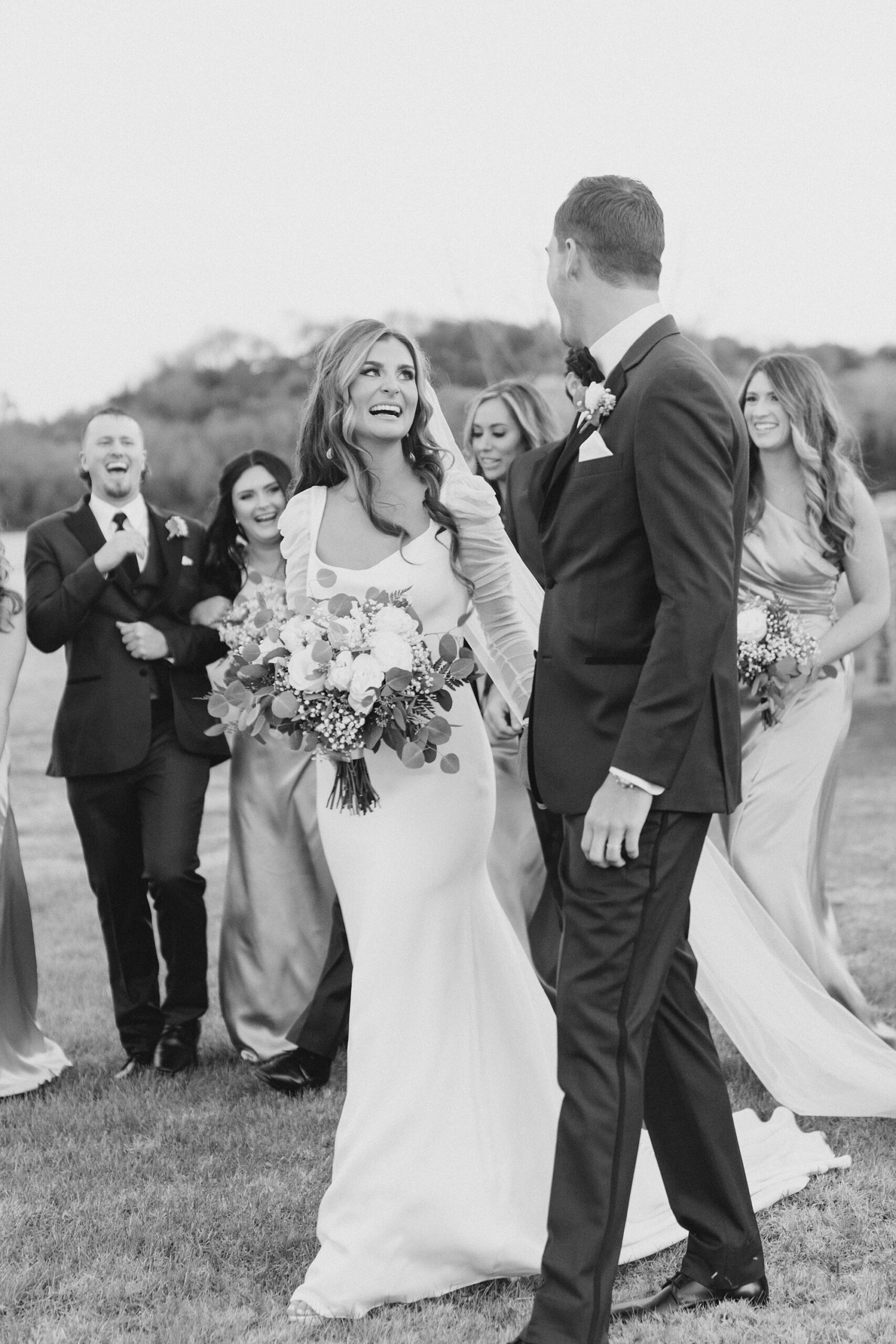 bride laughs up at groom walking with bridal party behind them 
