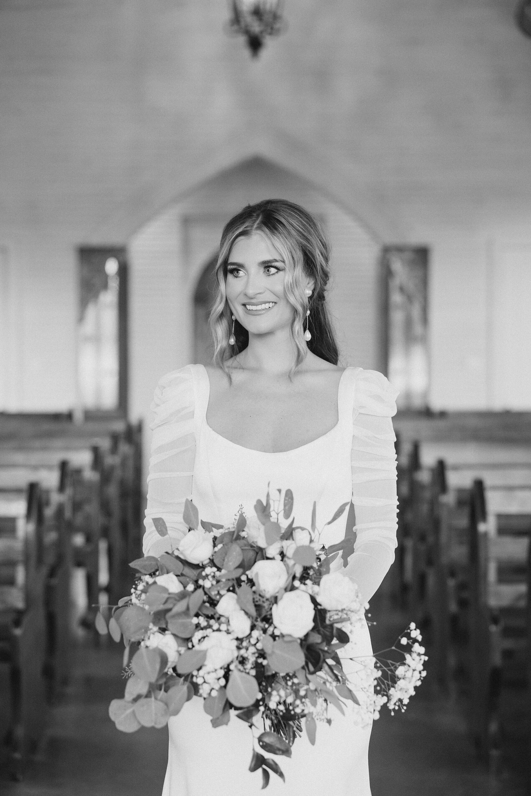 black and white portrait of bride smiling off to the side between wooden pews at The Brooks at Weatherford
