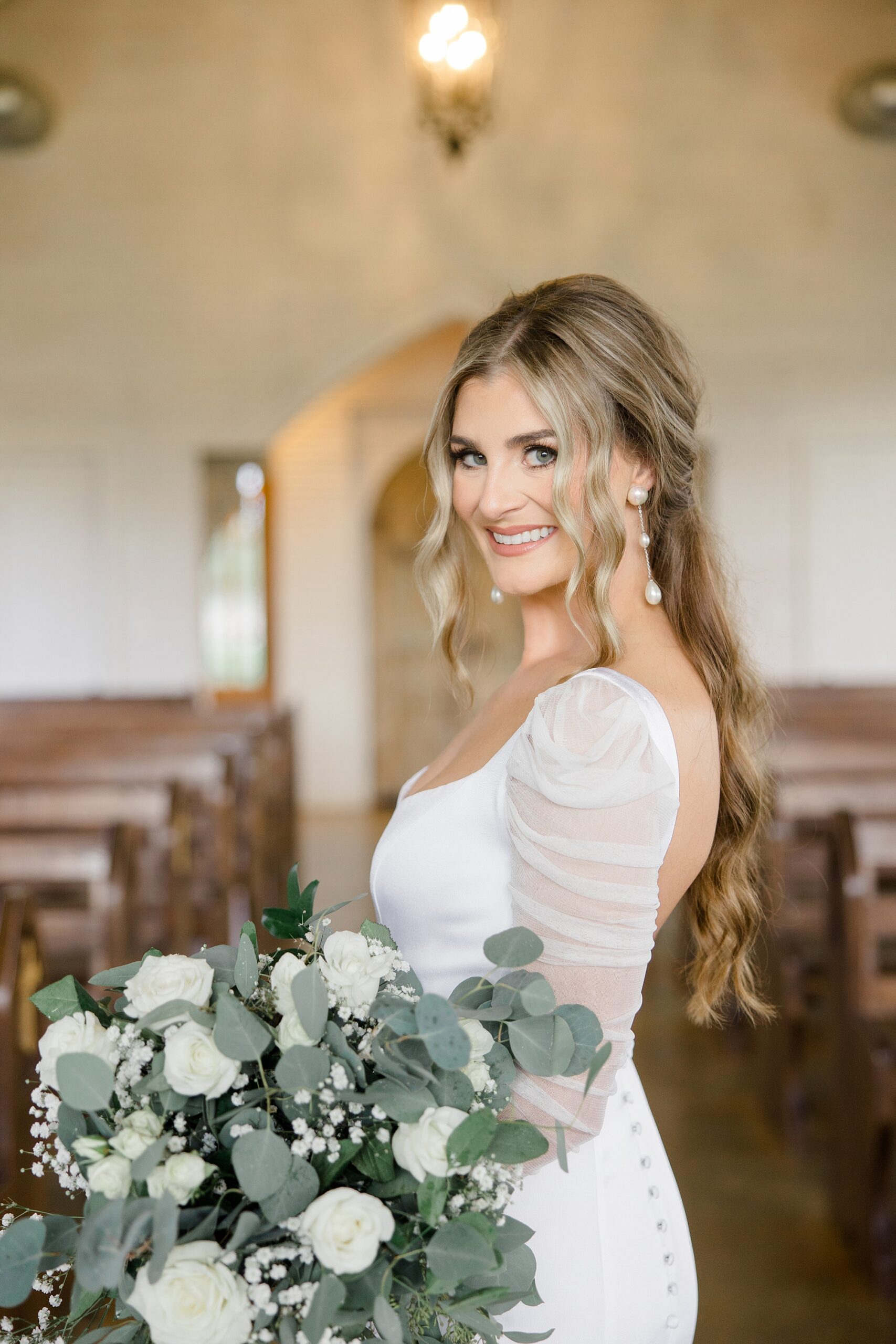 bride smiles over shoulder holding white flowers and eucalyptus bouquets 