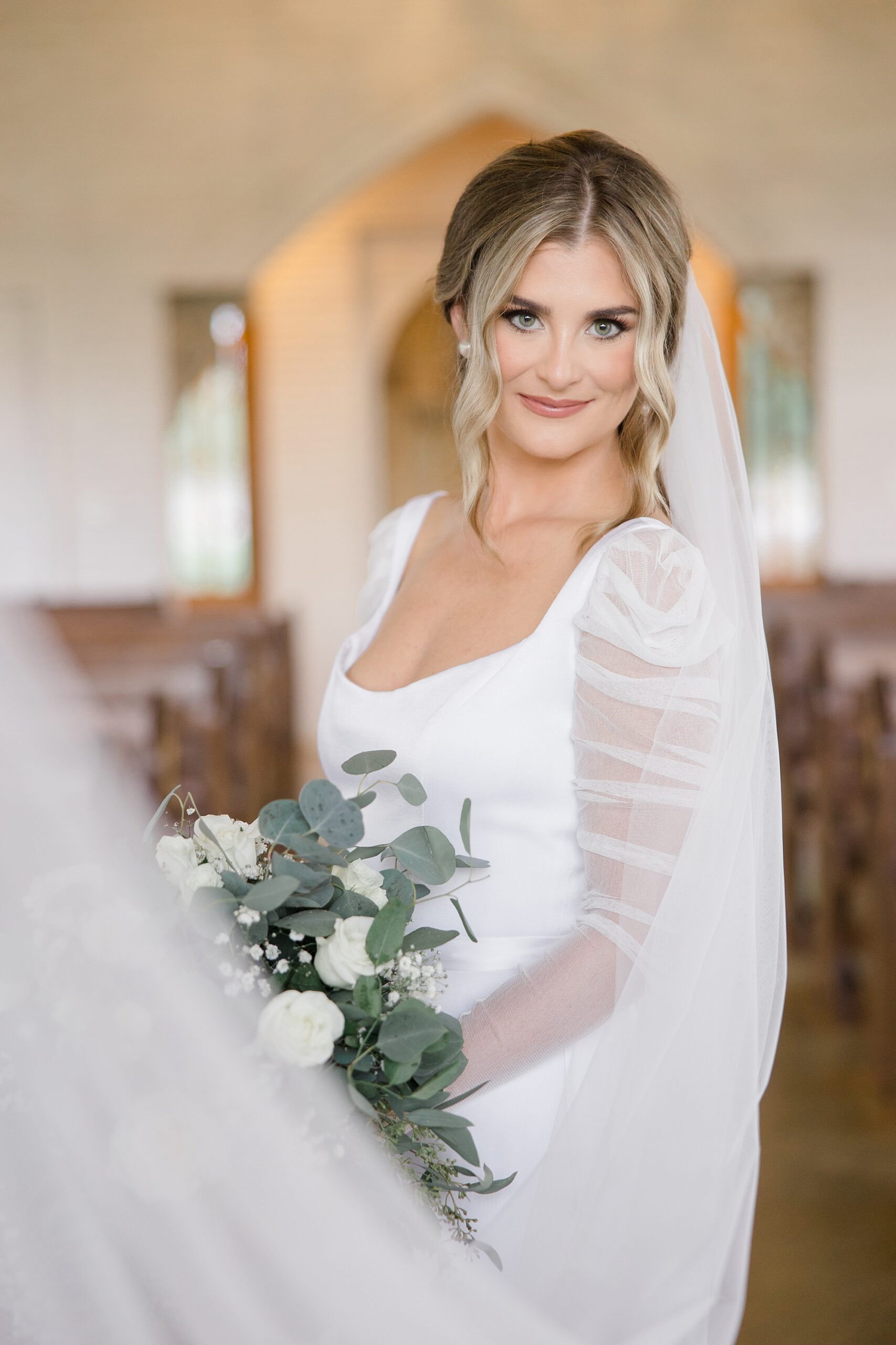 bride smiles holding bouquet of white flowers with veil around her