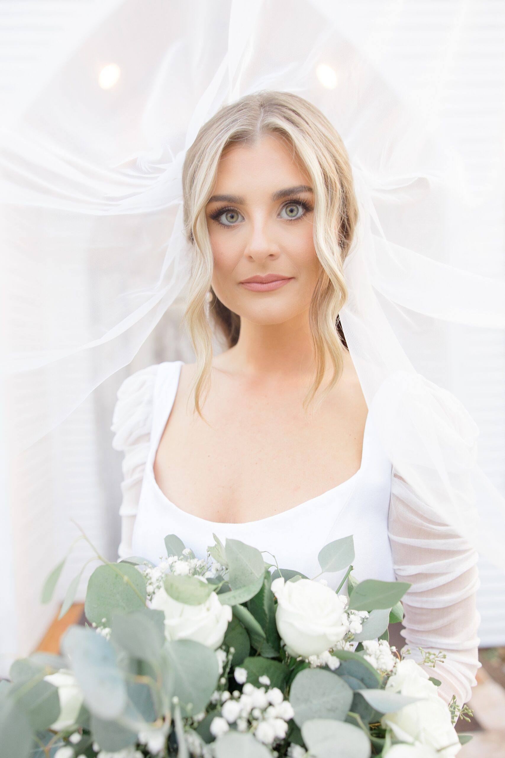 bride stand with veil lifted around her head with bouquet of white flowers 