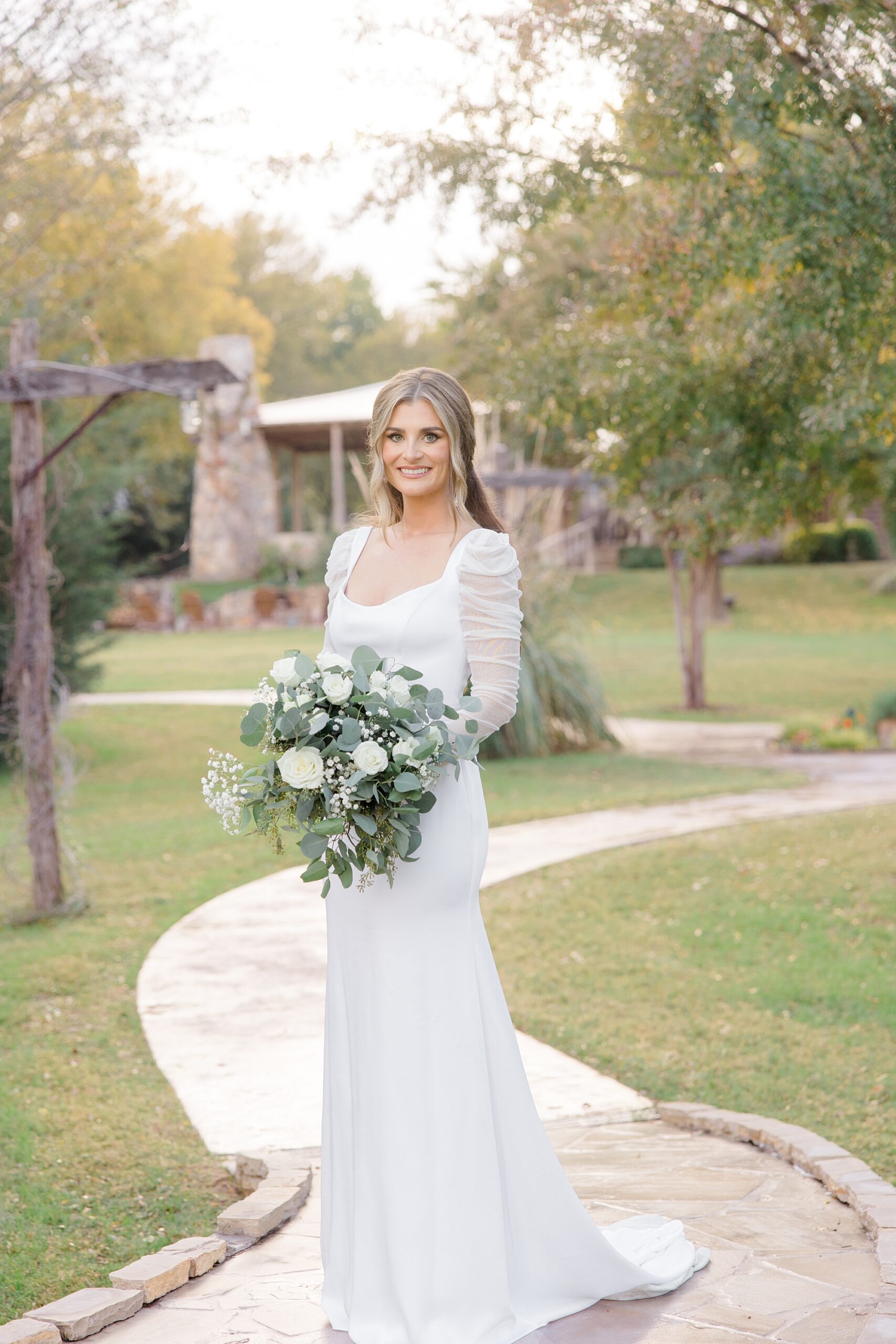 bride stands on brick pathway with white floral bouquet