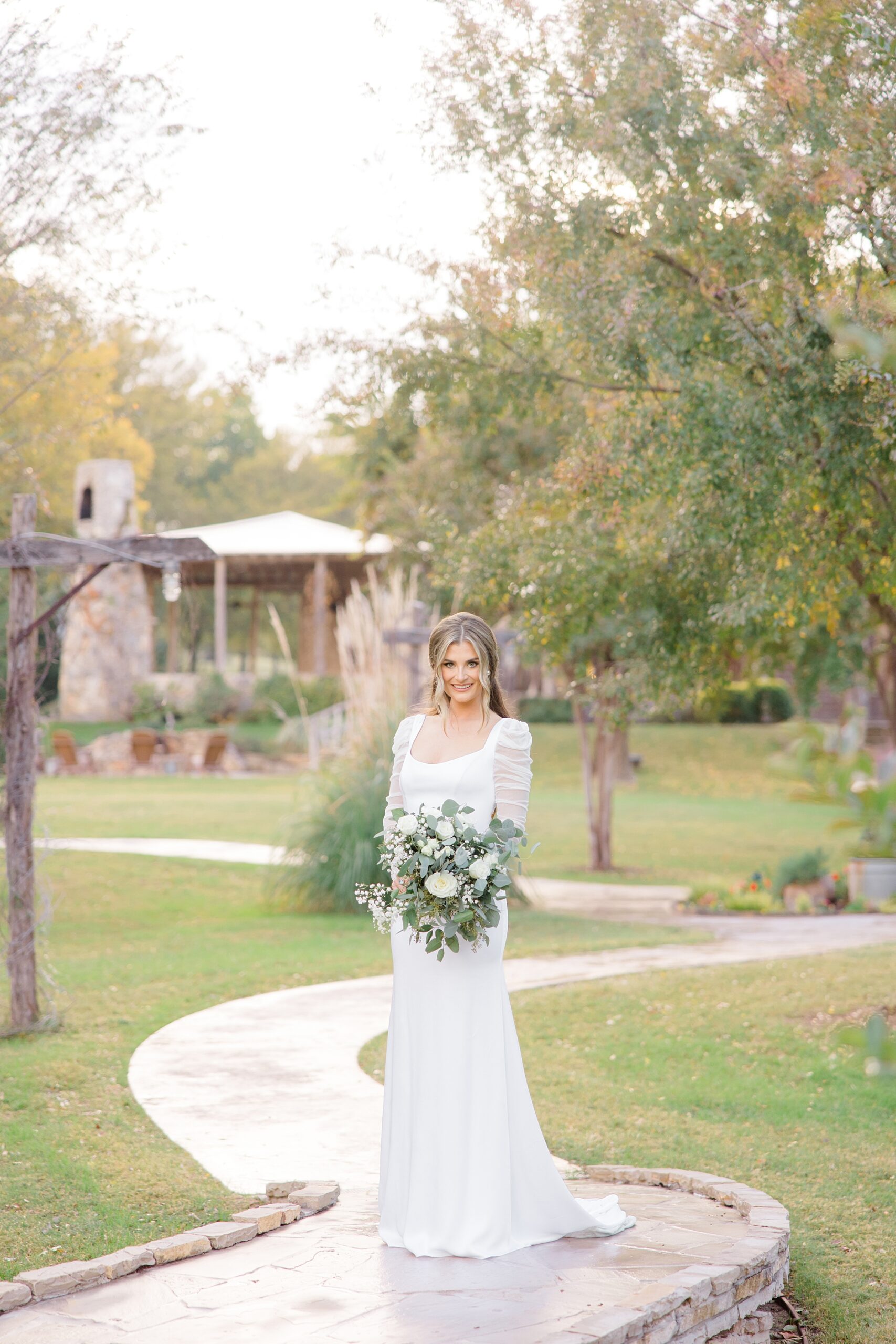 bride holds bouquet of white flowers on walkway through The Brooks at Weatherford