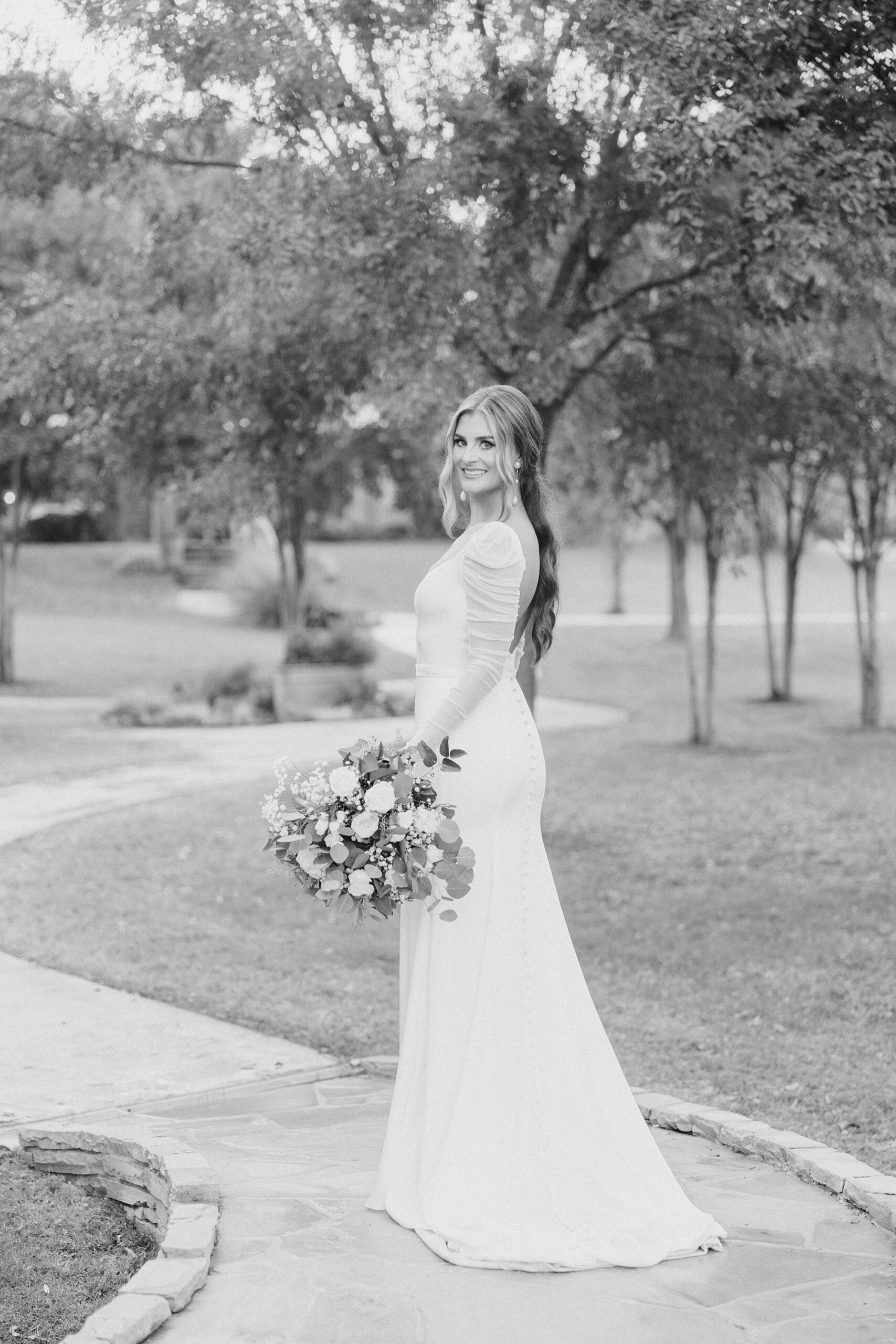 bride holds bouquet next to hip walking down path at The Brooks at Weatherford