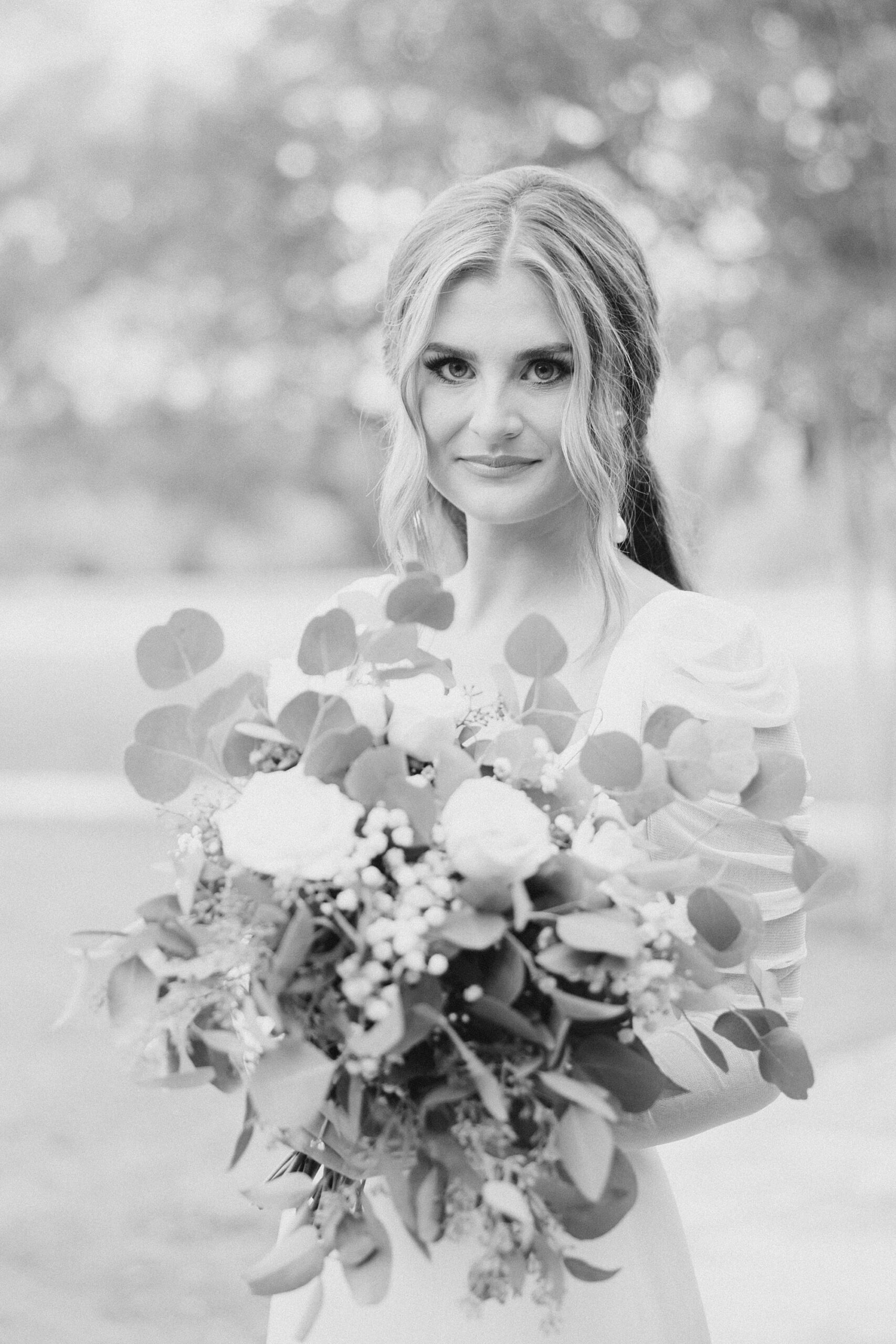 bride holds bouquet of white flowers and green leaves 
