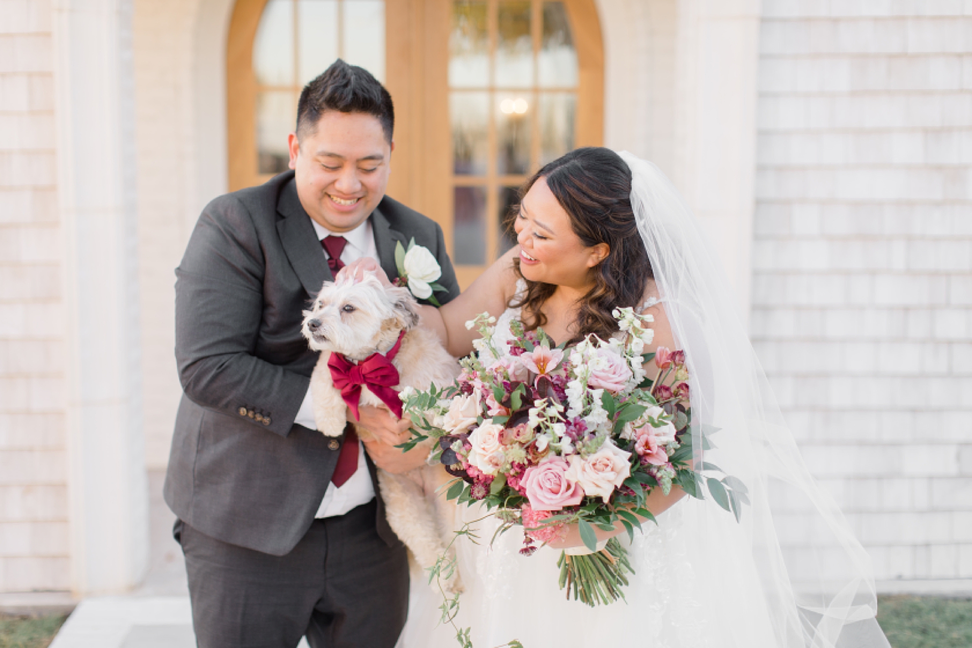 bride and groom laugh smiling at dog in groom's arms 