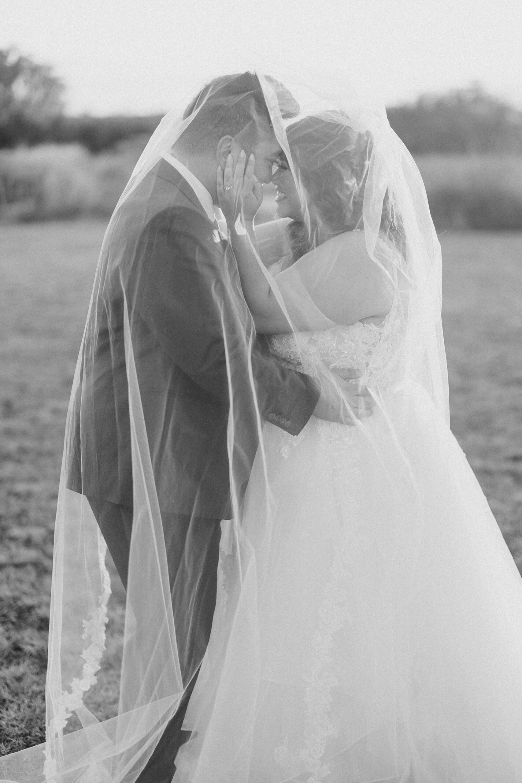 newlyweds hug under bride's veil on lawn at The Nest at Ruth Farms