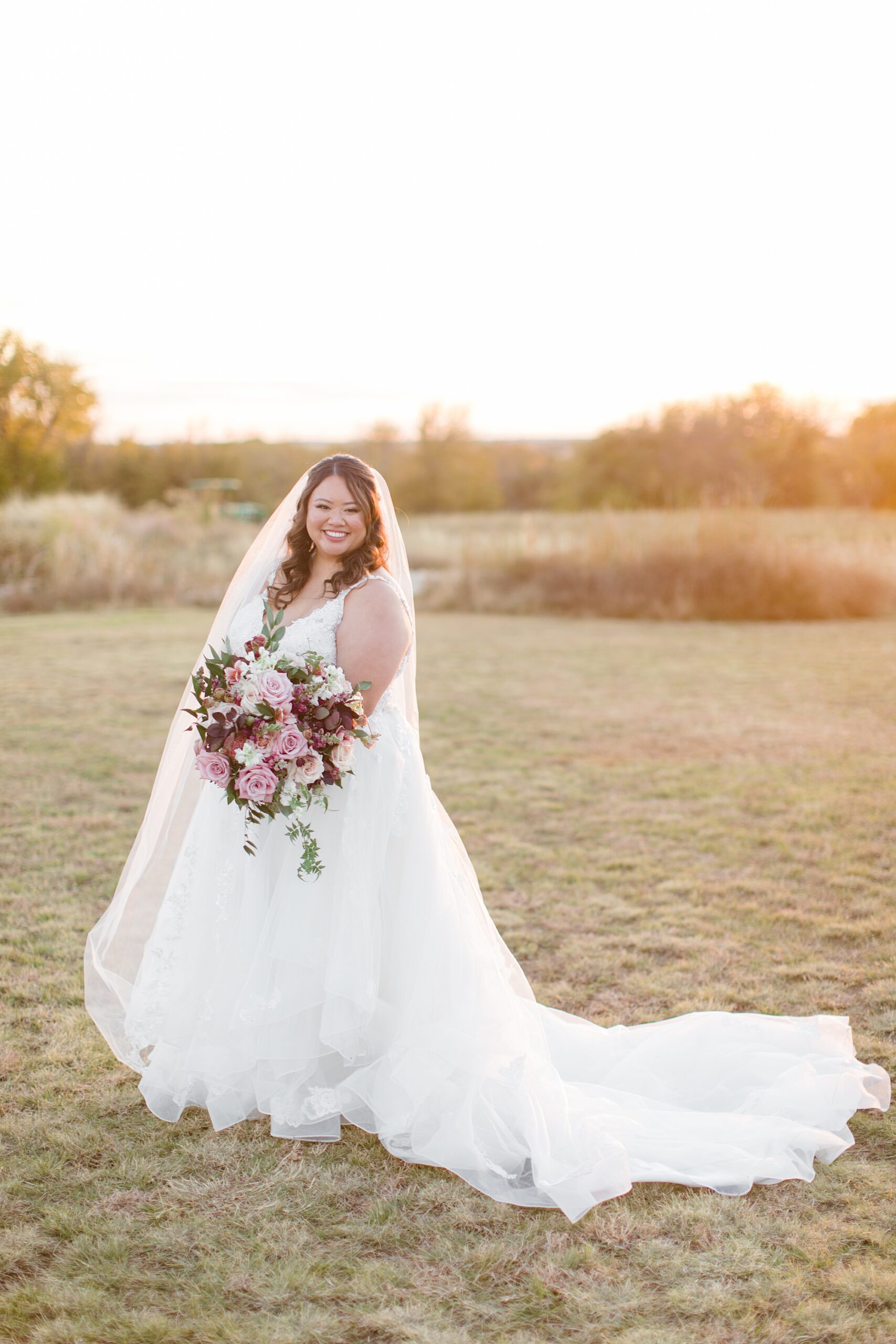 bride stands on lawn holding bouquet of pink roses at The Nest at Ruth Farms 