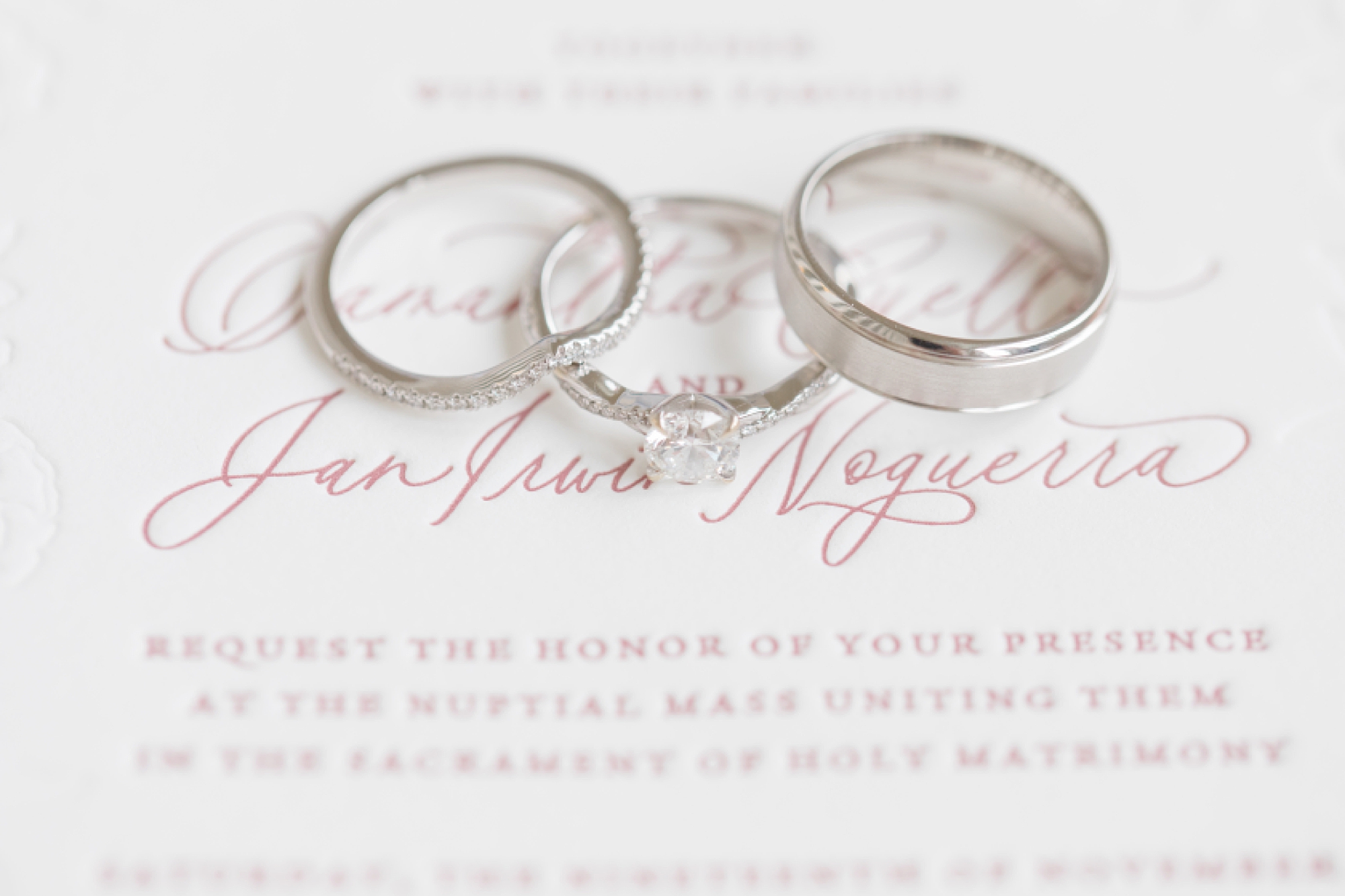 wedding rings lay on white invitation with pink lettering 