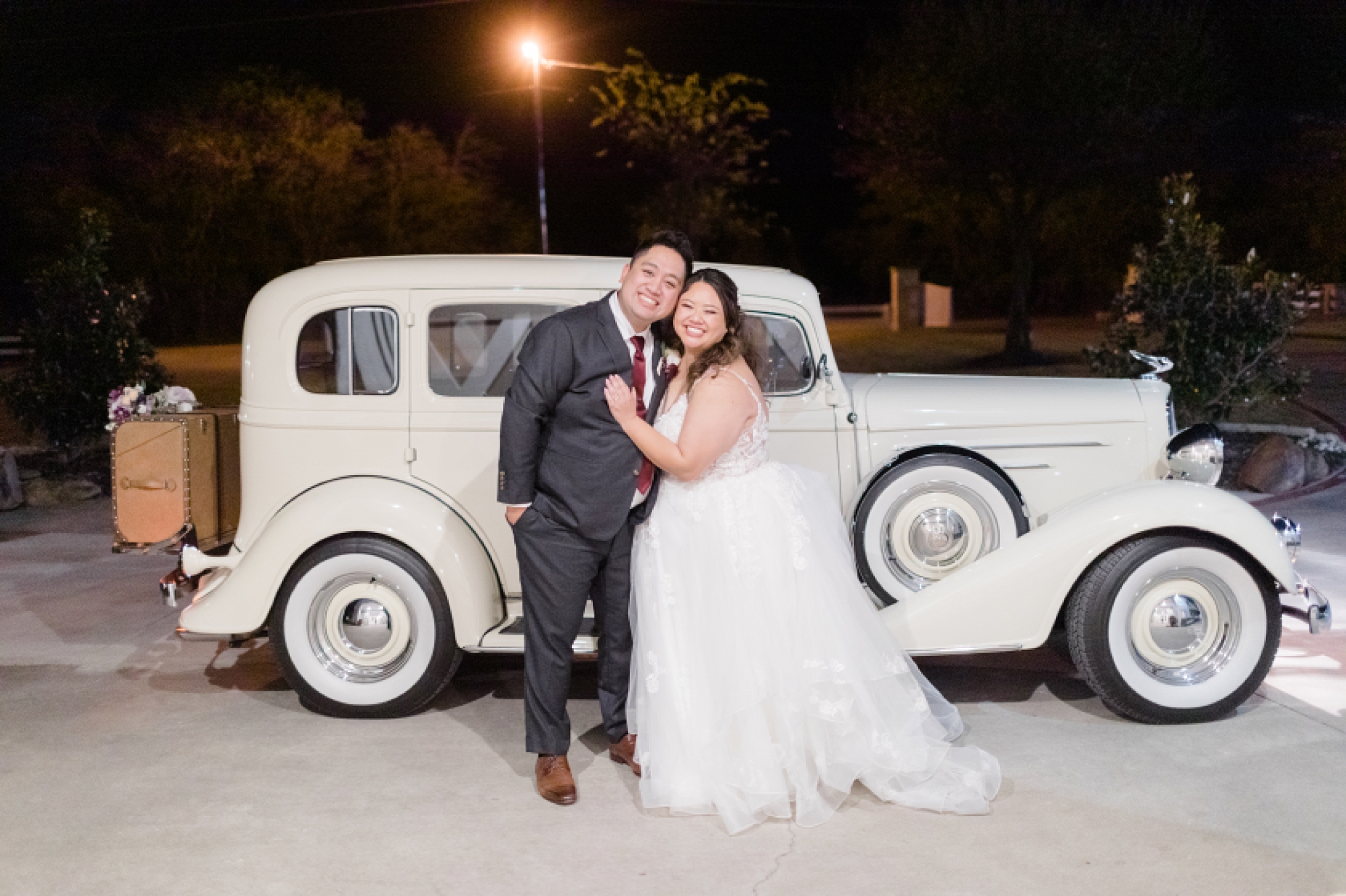 bride and groom pose by antique car outside Texas venue 