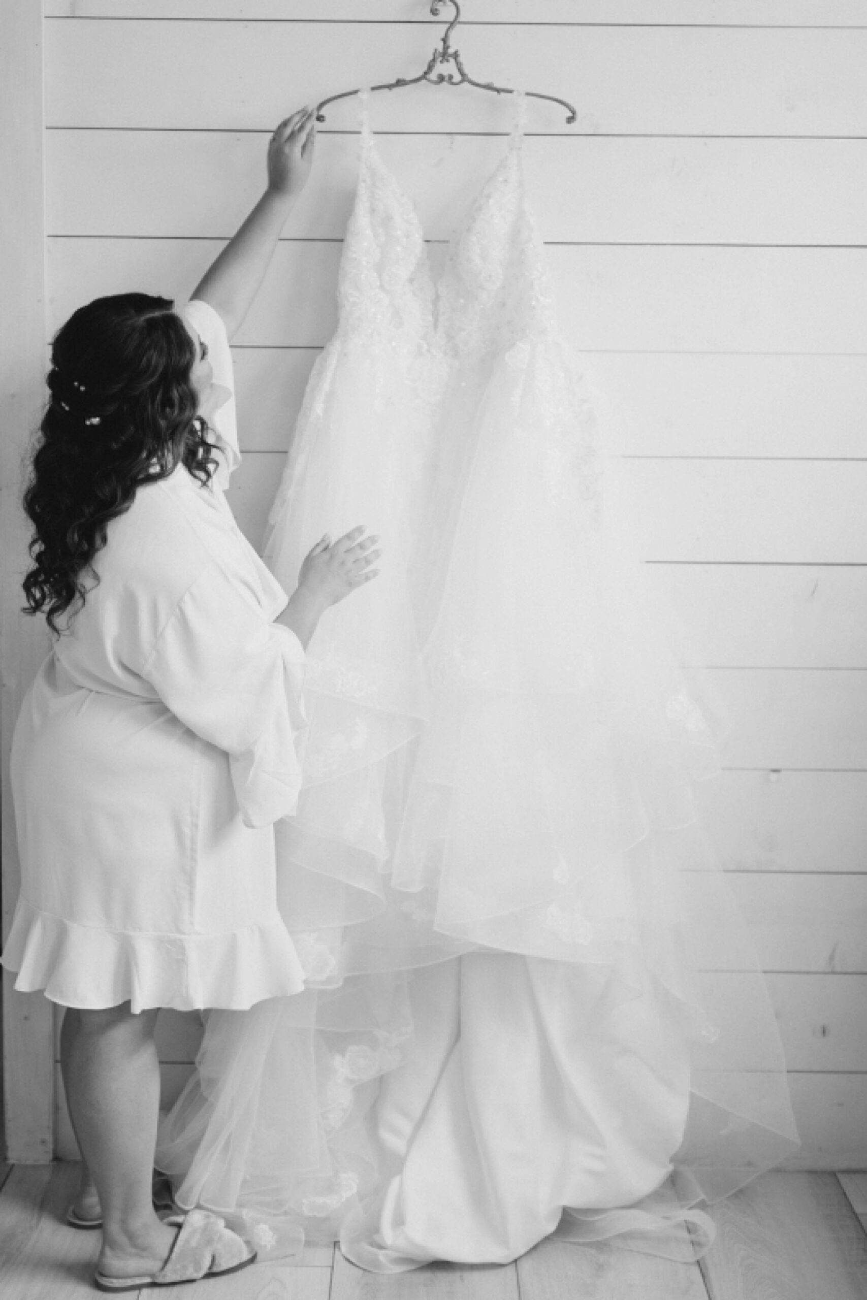 bride looks at wedding gown hanging on shiplap wall at The Nest at Ruth Farms