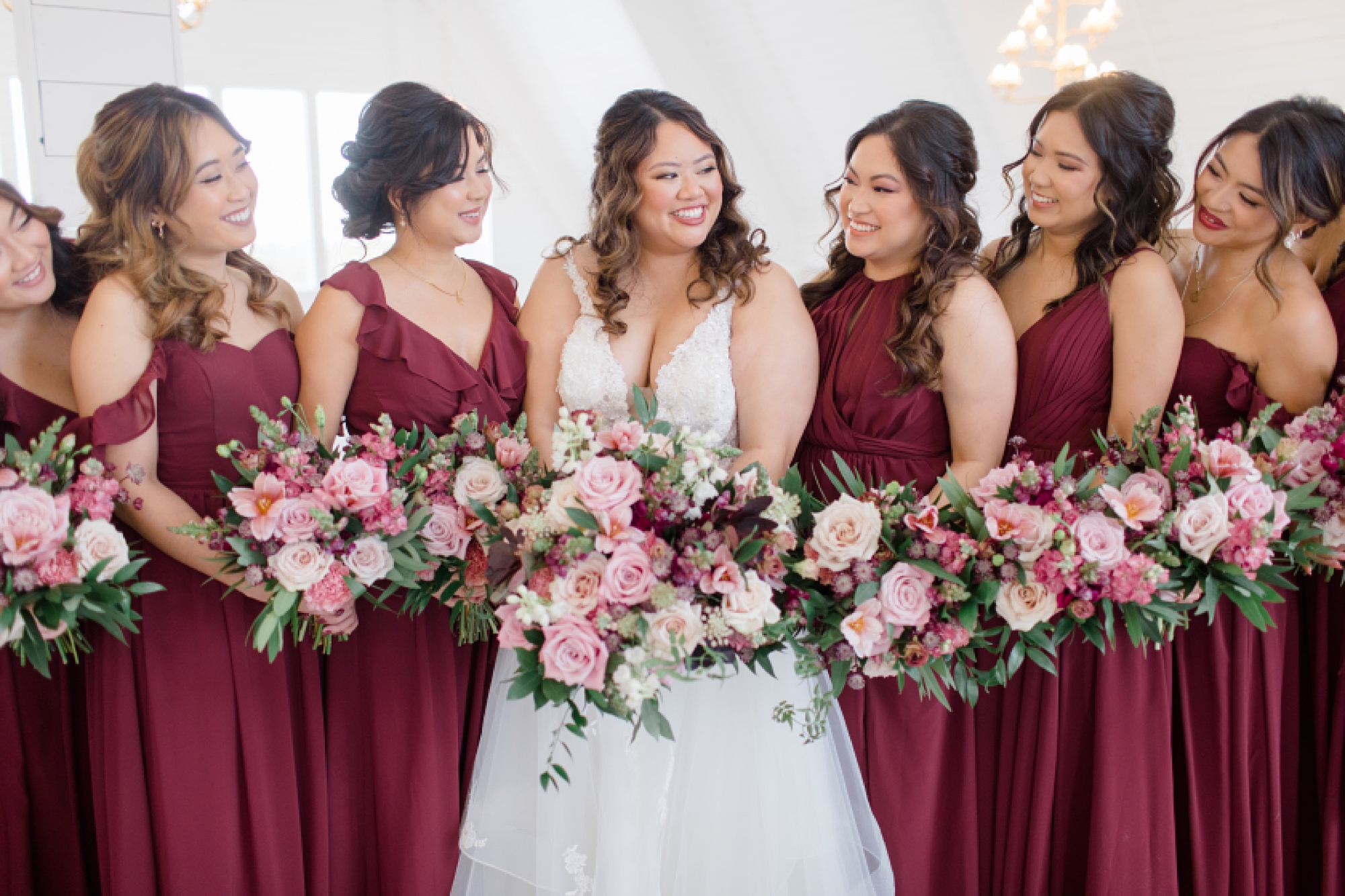 bride smiles at bridesmaids in burgundy gowns with pink flowers 