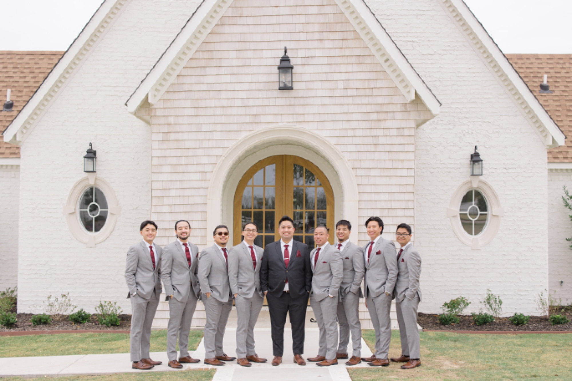 groom stands with groomsmen in grey suits in front of Frisco TX church