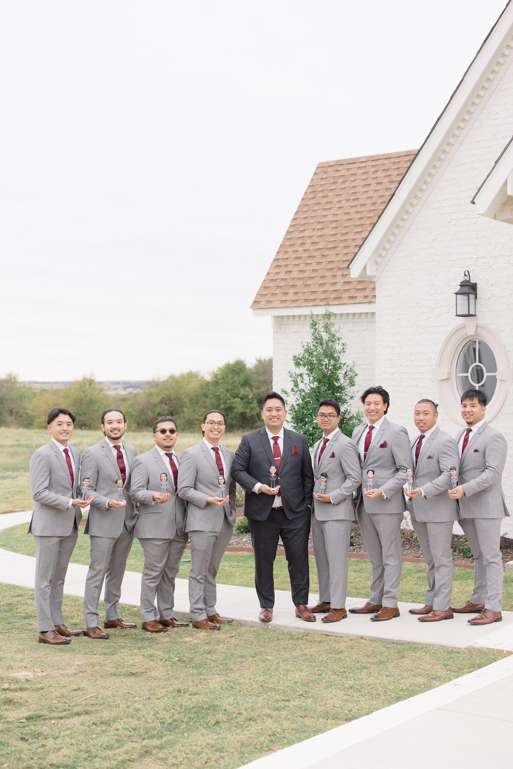 groom stands holding bobble head with groomsmen 