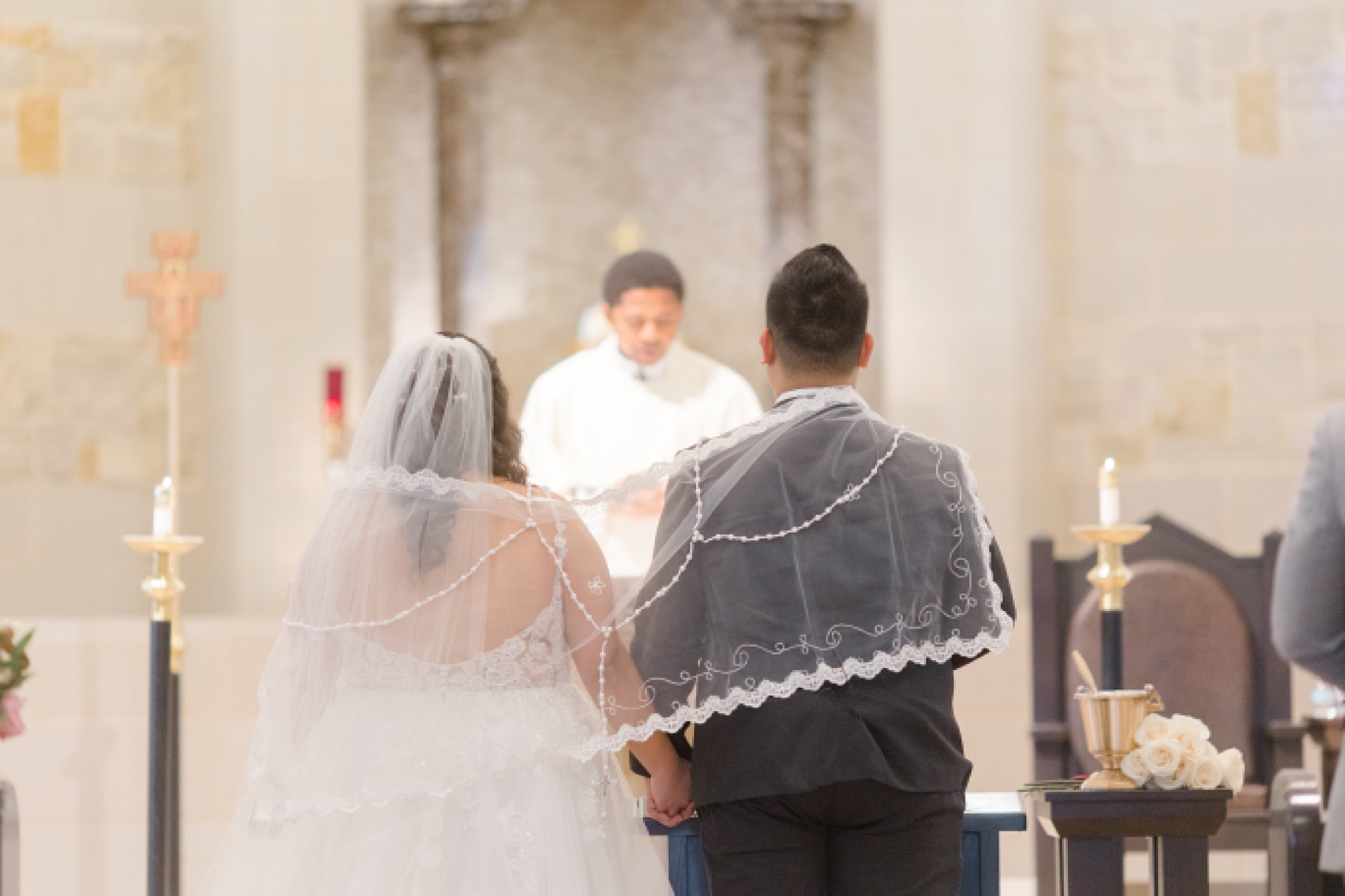 newlyweds stand under veil during ceremony at St. Francis of Assisi Catholic Church Frisco