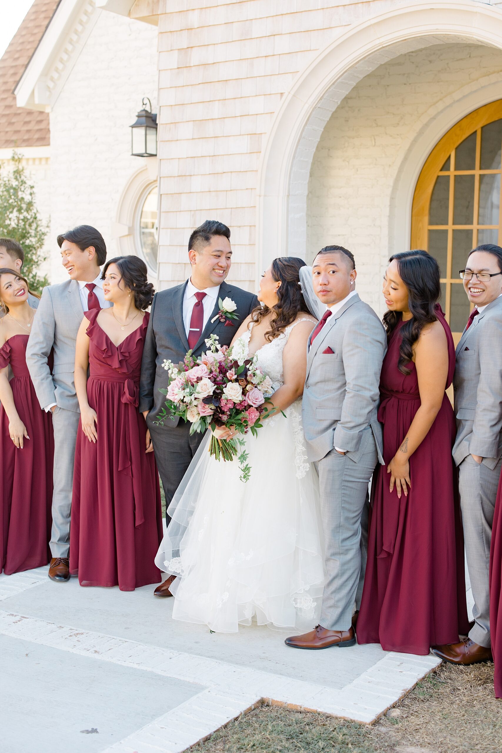 newlyweds pose with wedding party in burgundy and grey attire 