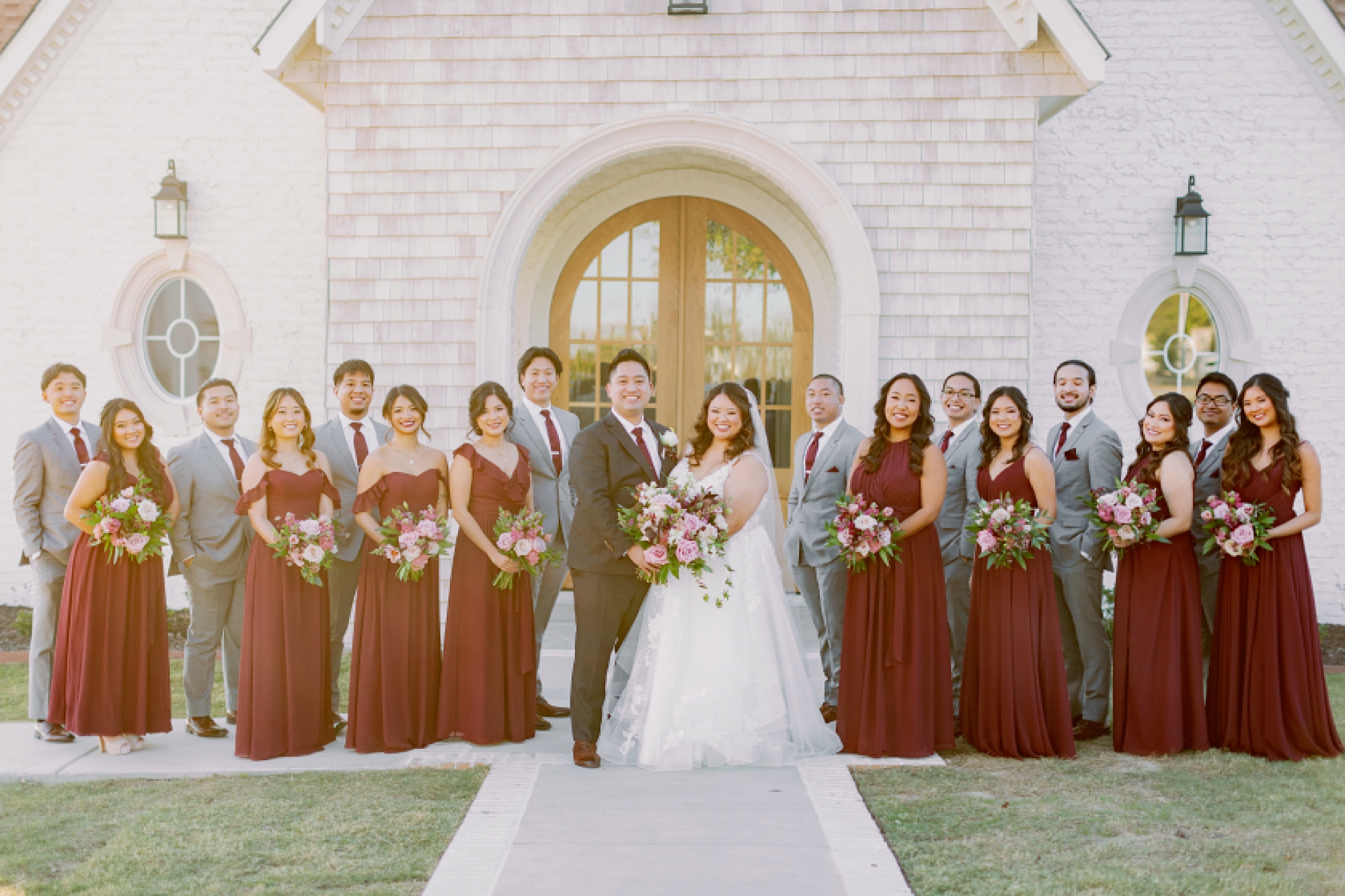 bride and groom pose with wedding party in burgundy gowns and grey suits 